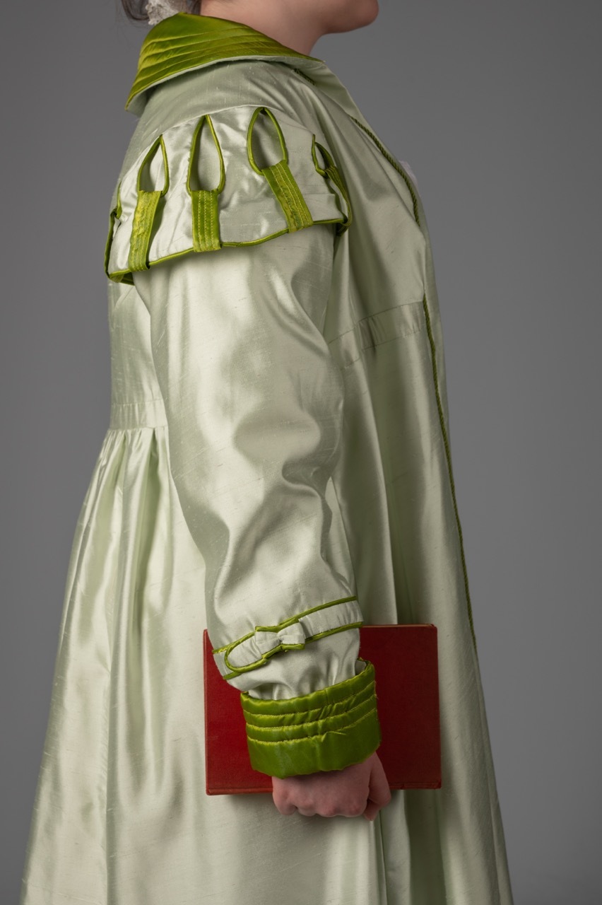 Pale green silk dress with bright green trim on collar, sleeves and cuffs. Person holds red clutch bag against grey background.