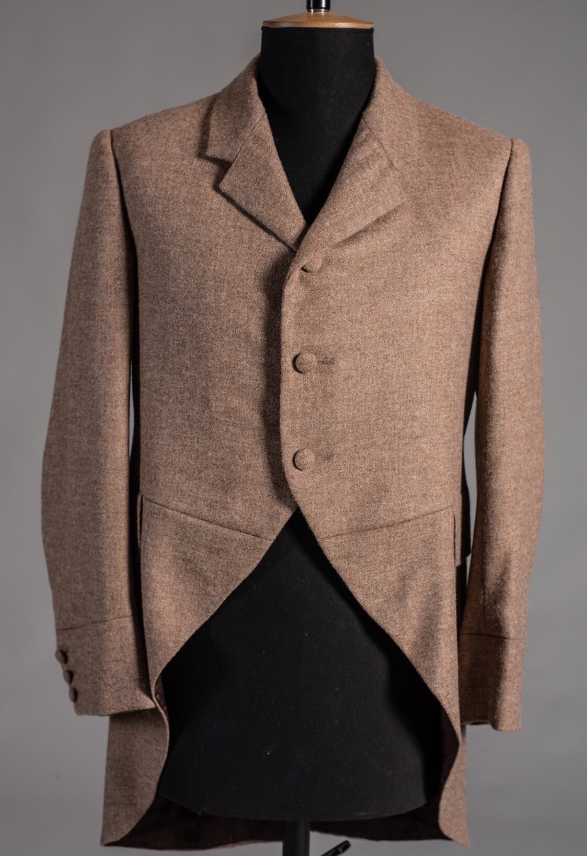 Brown tweed tailcoat with three buttons displayed on black dress form against grey background.