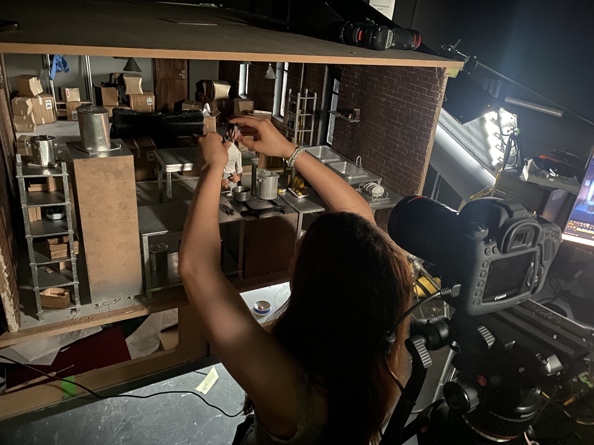 Person operating film projector equipment in dimly lit projection booth with mechanical components and bright lamp illumination.