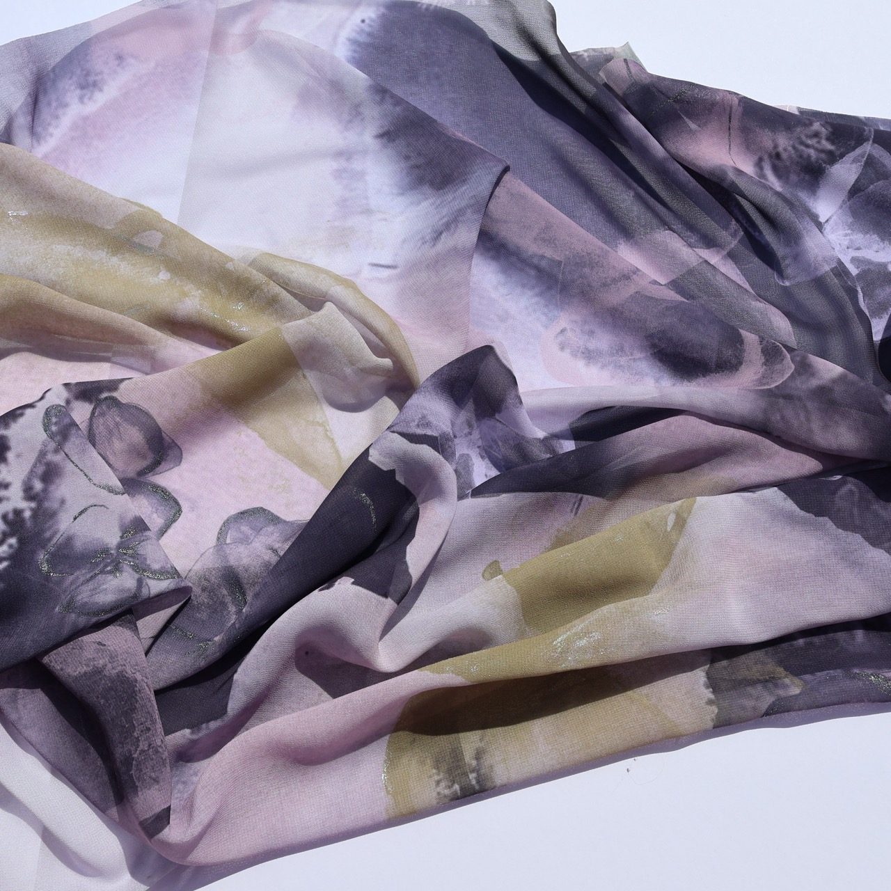 A flowing fabric with an abstract design featuring soft hues of pink, lavender, and light grey, intertwined with darker shades. The fabric is loosely arranged, showcasing its delicate texture and fluid appearance.