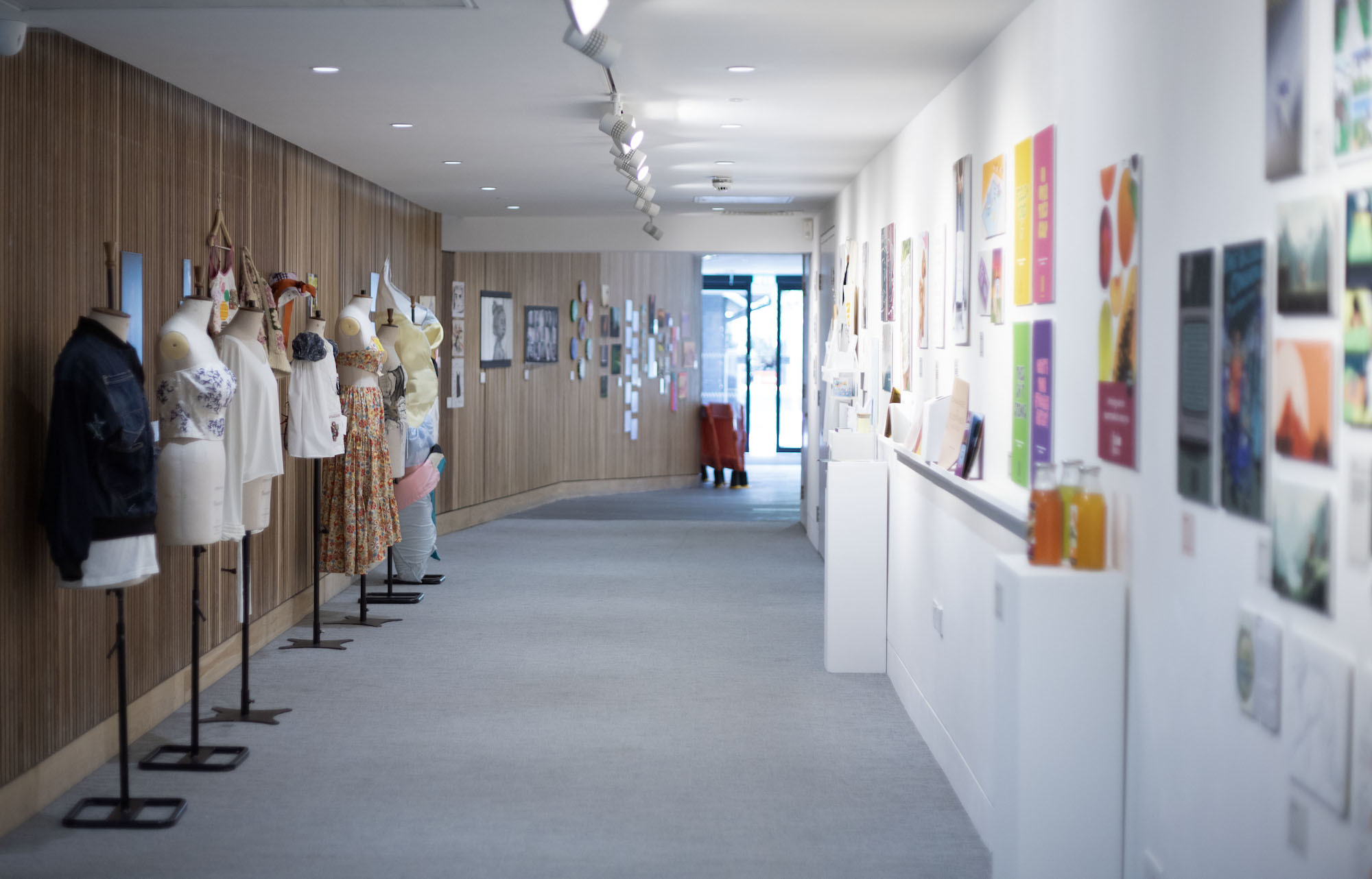 A hallway in TheGallery at AUB, a row of dressed mannequins lined up on the left, an assortment of artwork hanging on the right-hand wall.