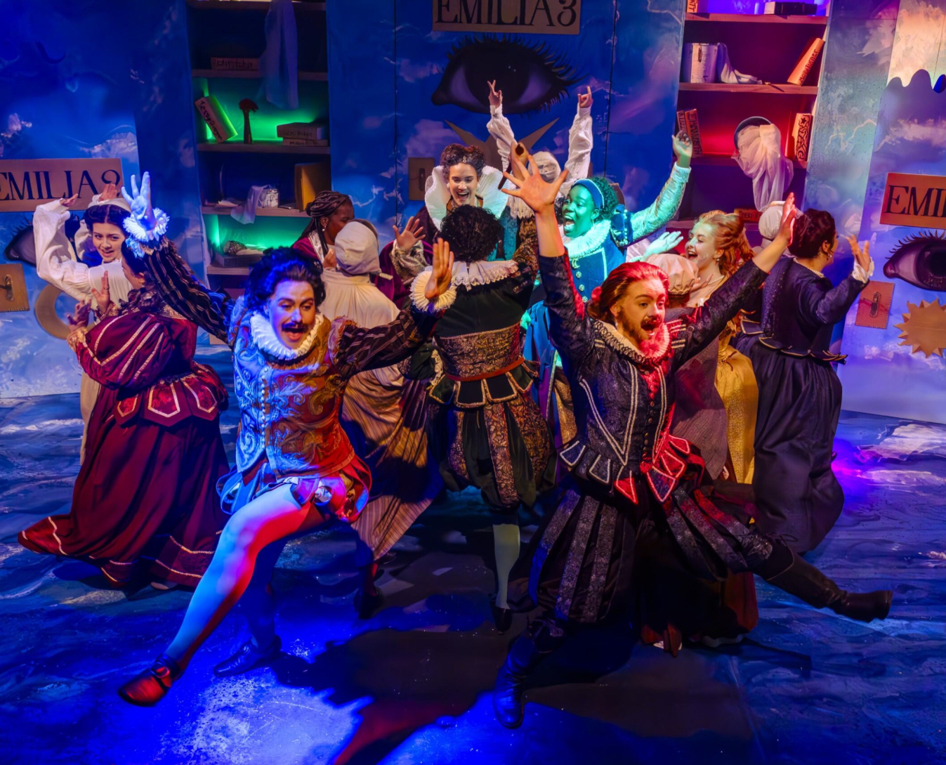 A group of BA (Hons) Acting students dressed in colourful 16th century costumes dance around a stage while performing in "Emilia!"