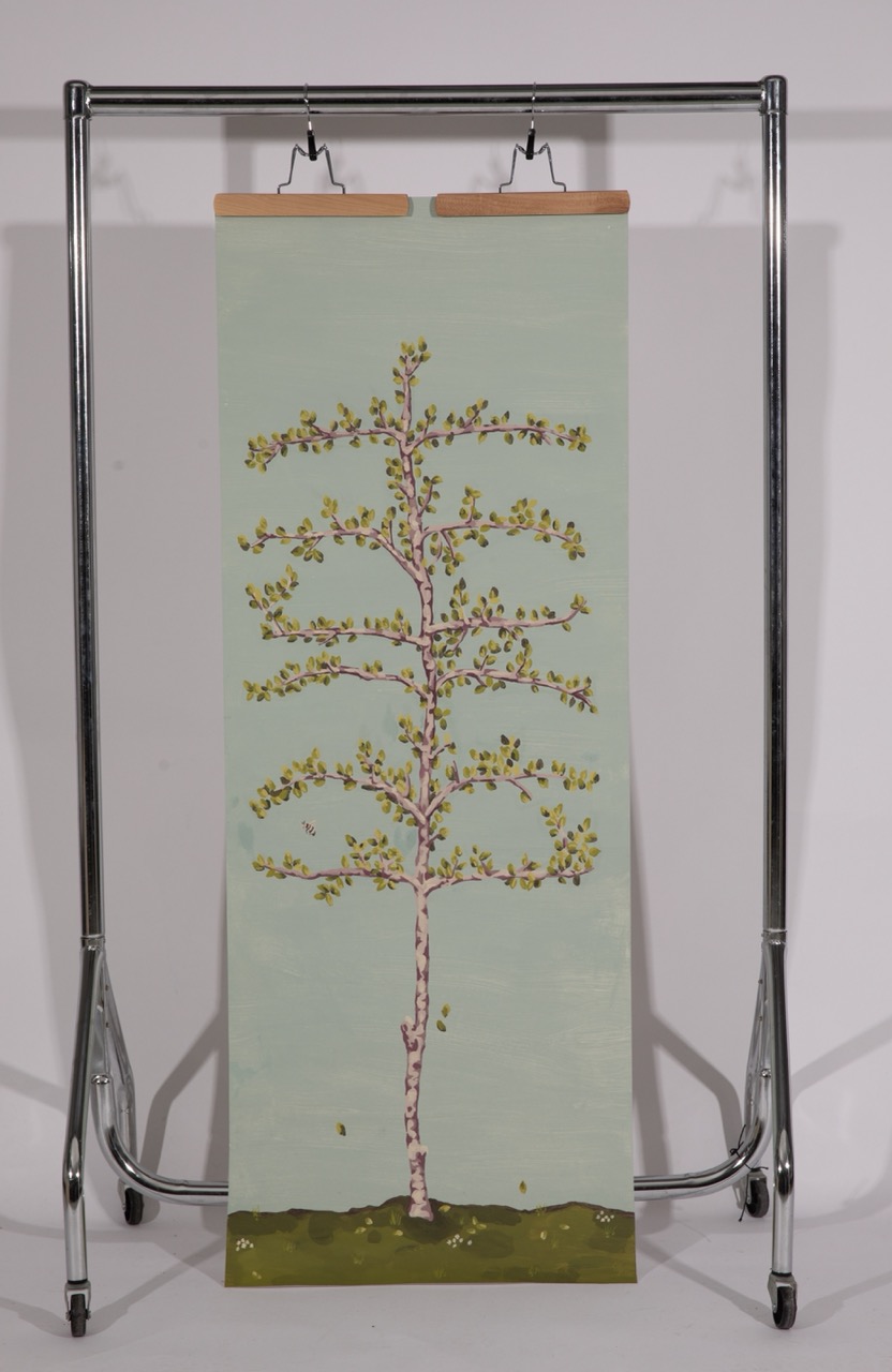 A vertical painting of a tree with a light blue background, displaying its branches adorned with leaves and pink blossoms. The artwork is hung from a metal display stand, featuring a green grassy base at the bottom.