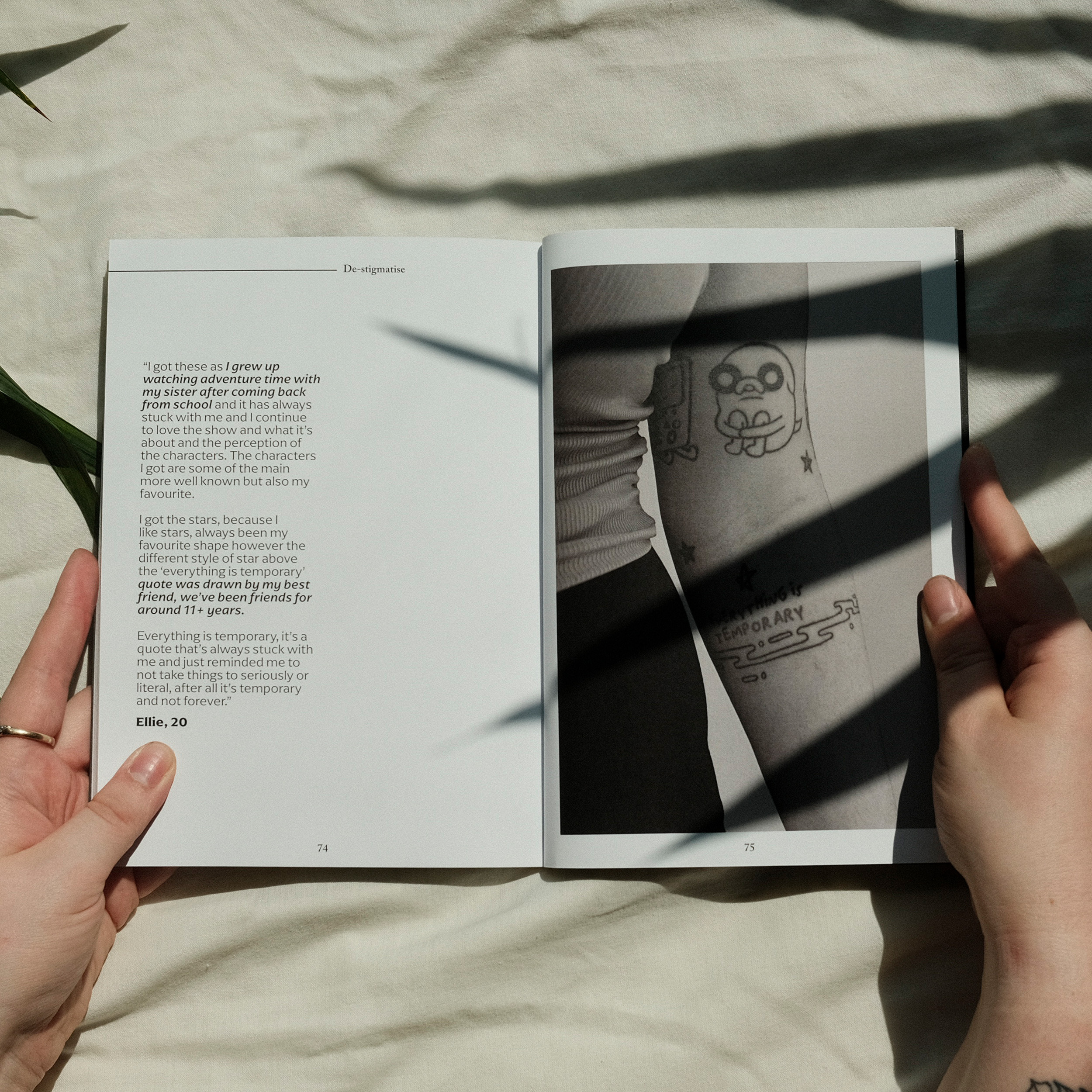 Open book held by hands showing text on left page and black and white photograph of person's torso with tattoo on right page.