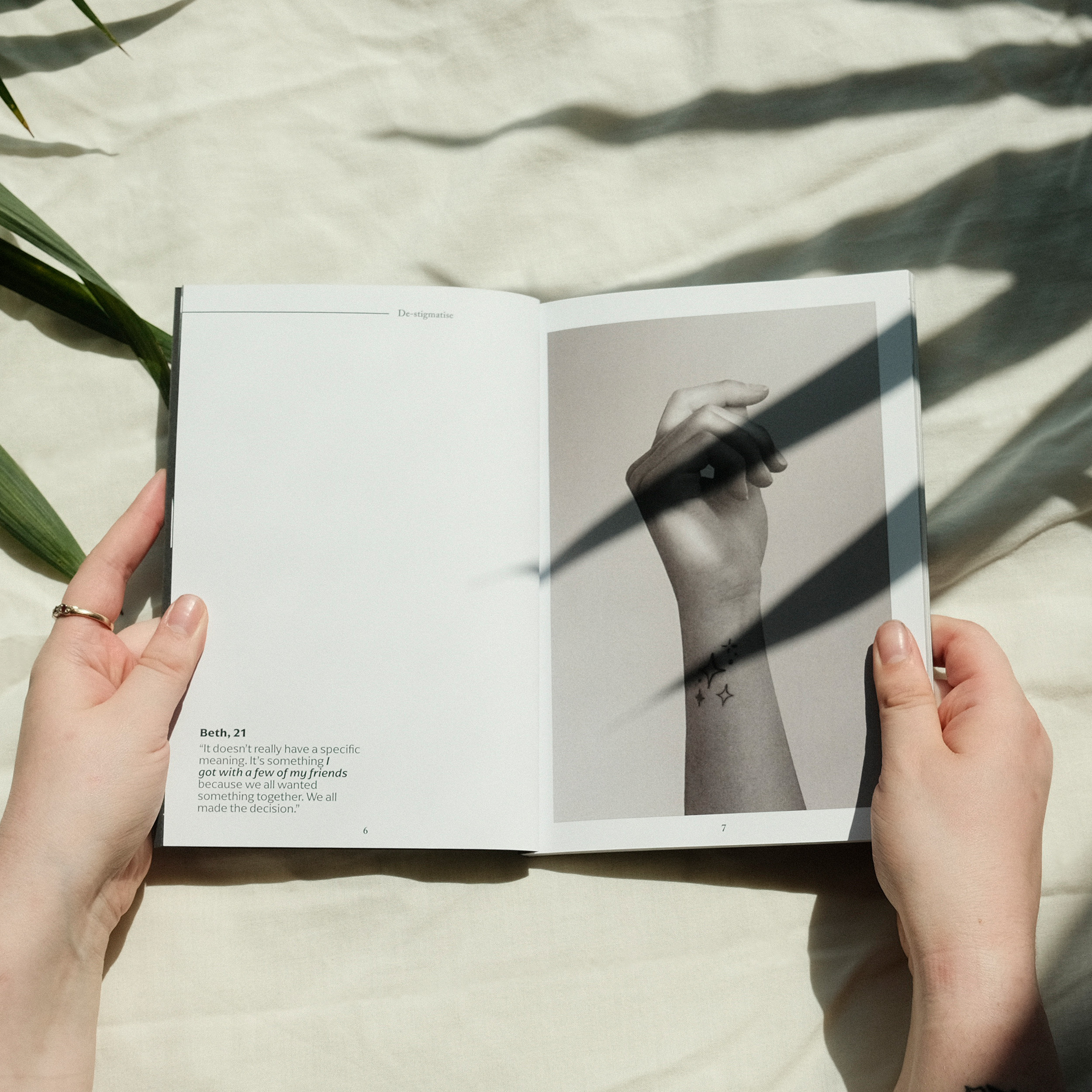 Open book held by hands showing text page and black and white portrait, with plant shadows casting dark stripes across white surface.