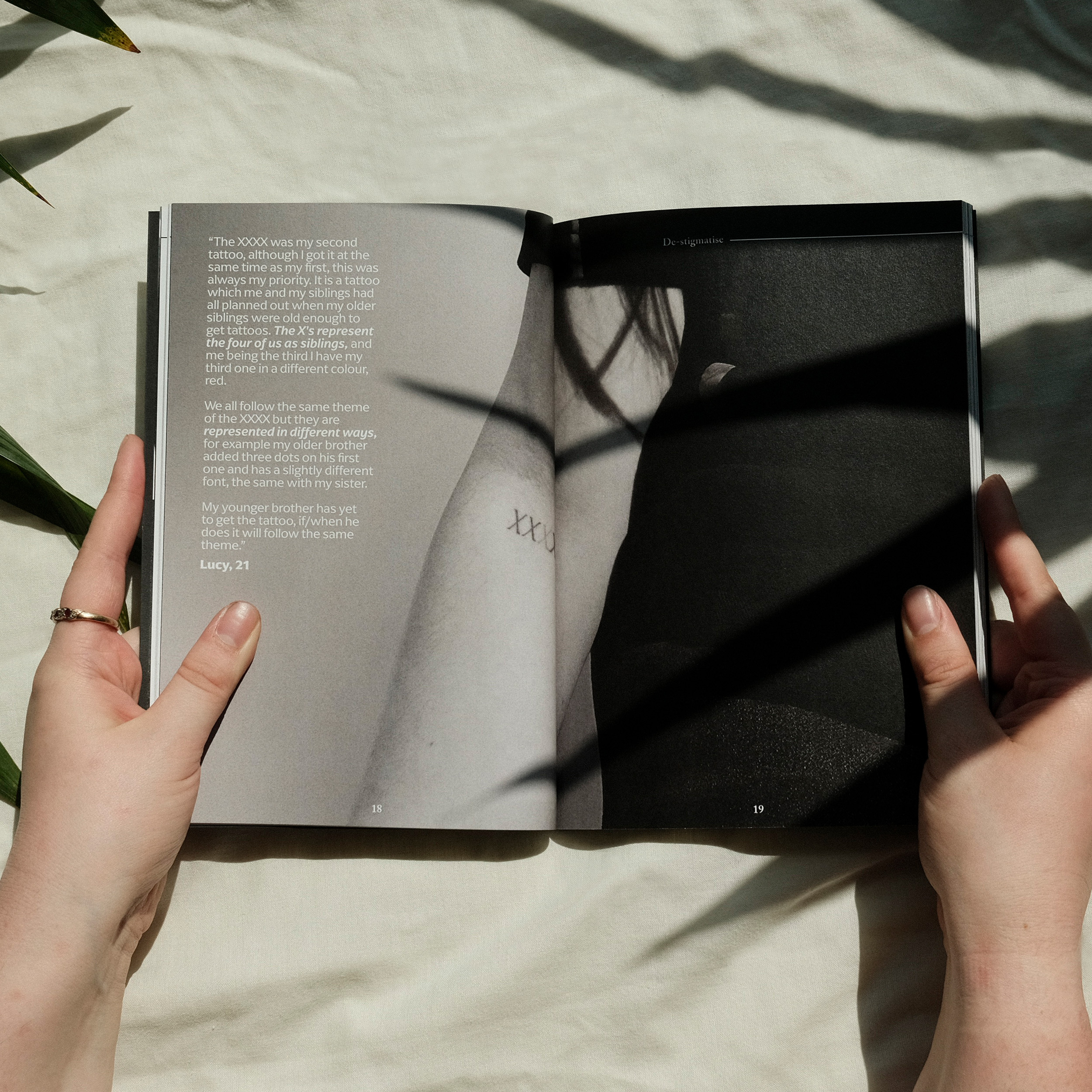 Hands holding open book with text on left page and black and white image of person in black clothing on right page.
