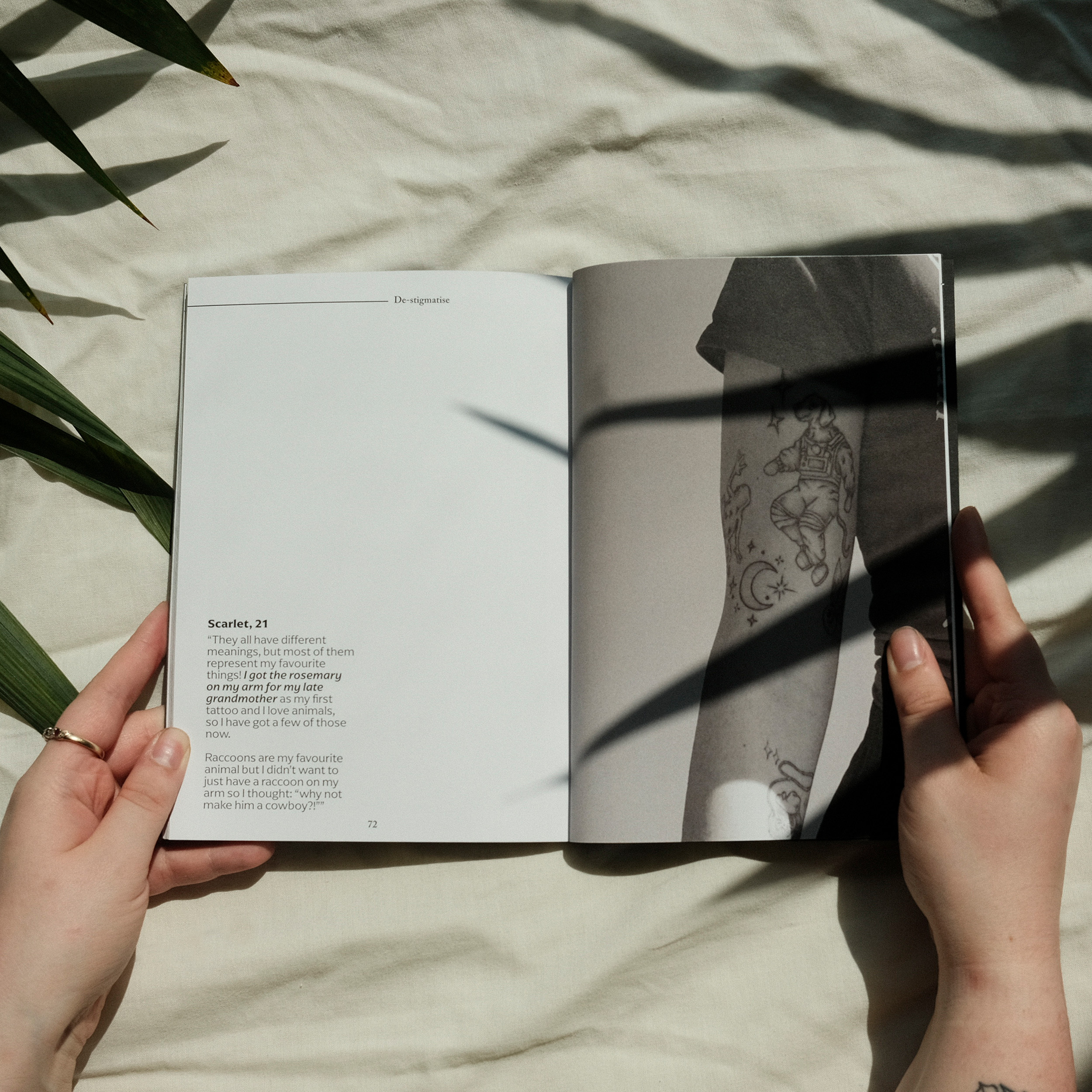 Hands holding open book with white pages and text, green plant shadows cast across white bedding surface.