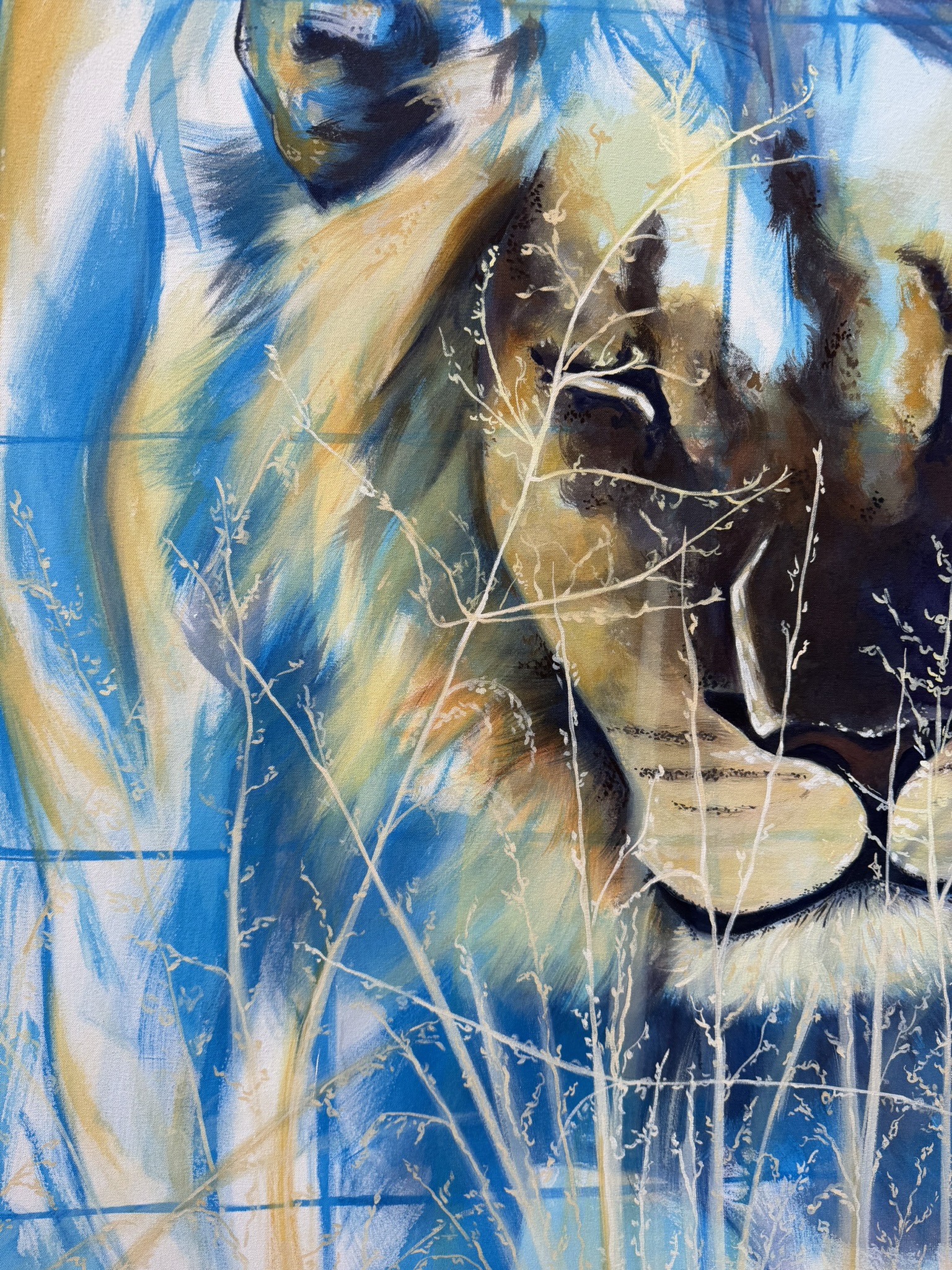 A close-up of a lion's face blended with abstract artistic elements, featuring shades of blue, gold, and cream. Delicate white plant silhouettes are presented in front of the lion, enhancing the contrast between the animal and the background.