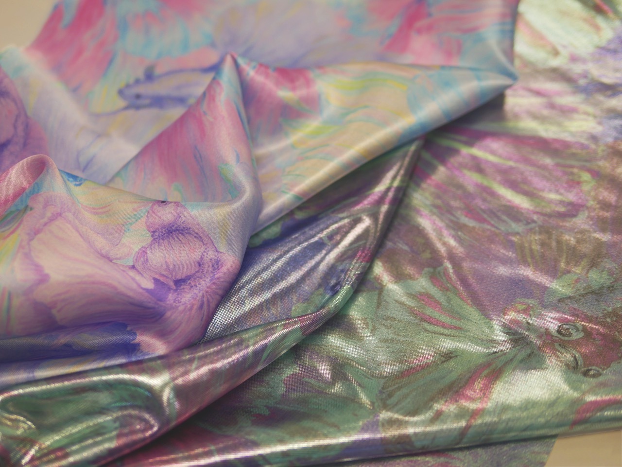 Crumpled iridescent fabric with purple, pink, green and silver tones creating angular folds and reflective surfaces.