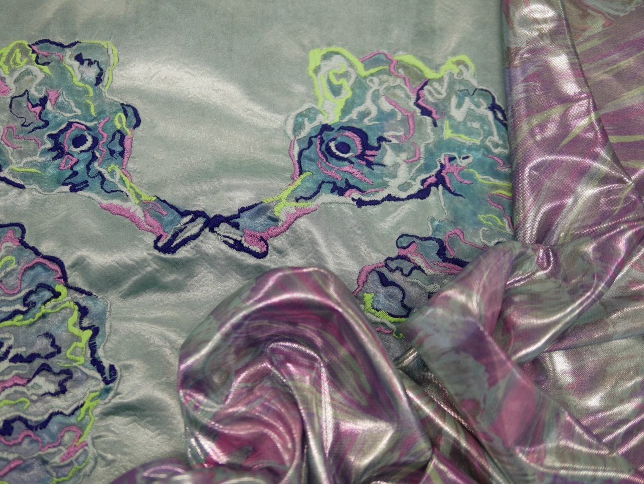 Illustration with flowing purple and pink fabric in foreground, green and purple organic shapes in background on pale green surface.