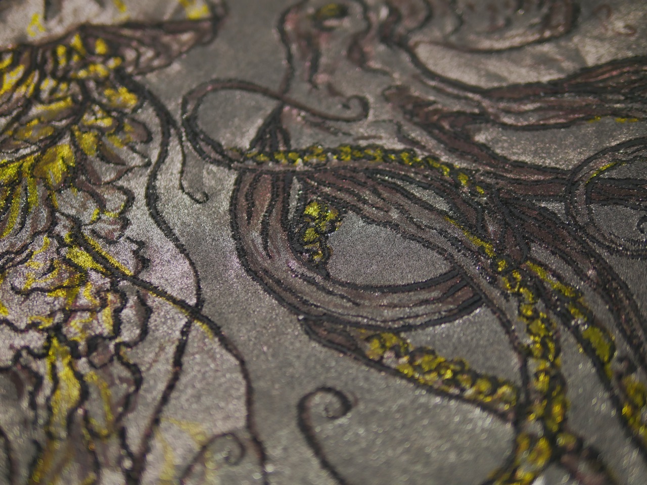 Intricate carved stone surface with flowing curved lines and swirls, featuring grey tones with bright yellow-green moss or lichen accents.
