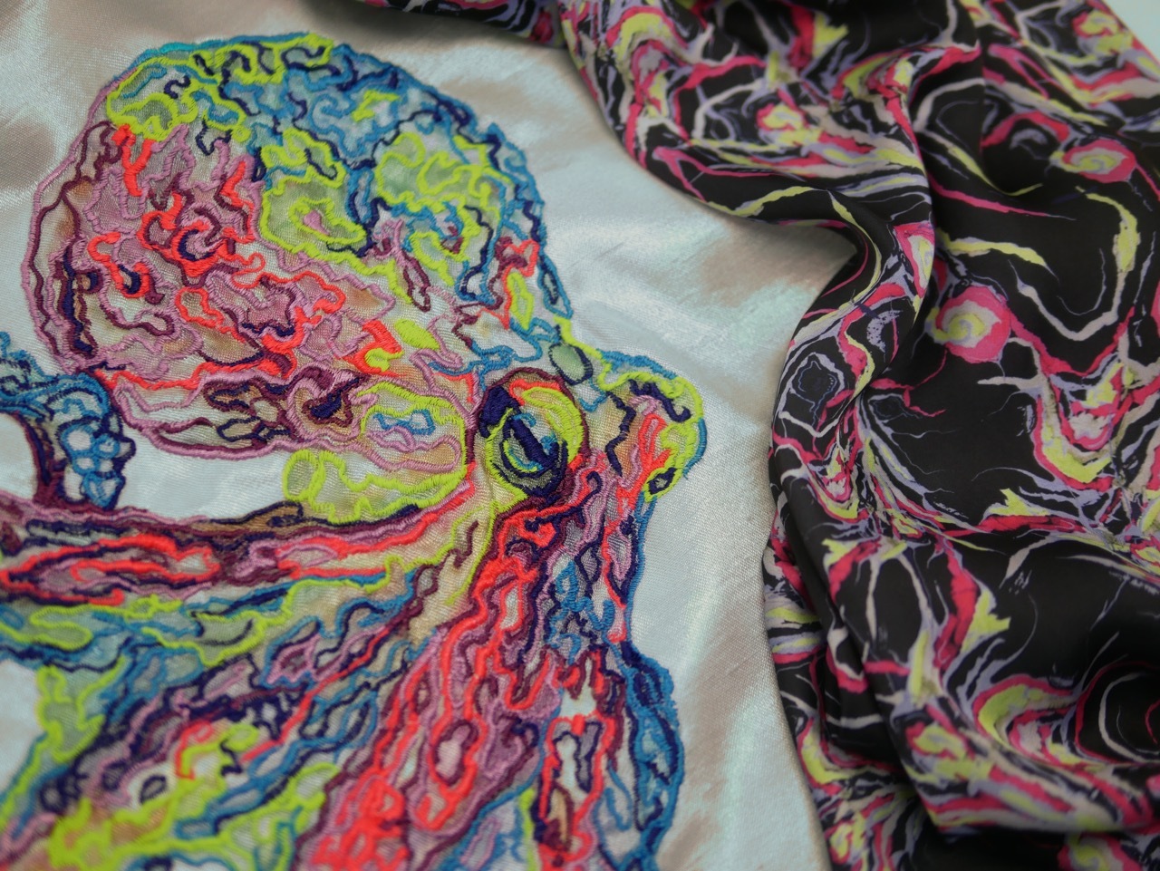 Colourful fabric with swirling patterns in bright greens, reds, blues and purples alongside dark fabric with pink and yellow swirled designs.