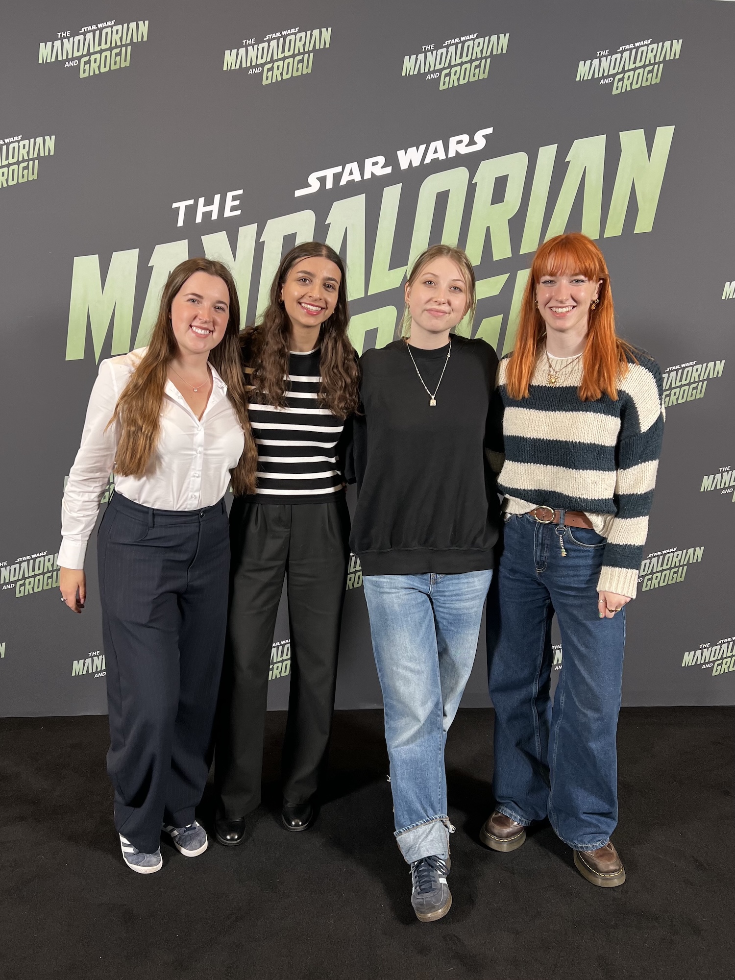 Four young people stand together in front of a Star Wars: The Mandalorian and Grogu backdrop at a promotional event.