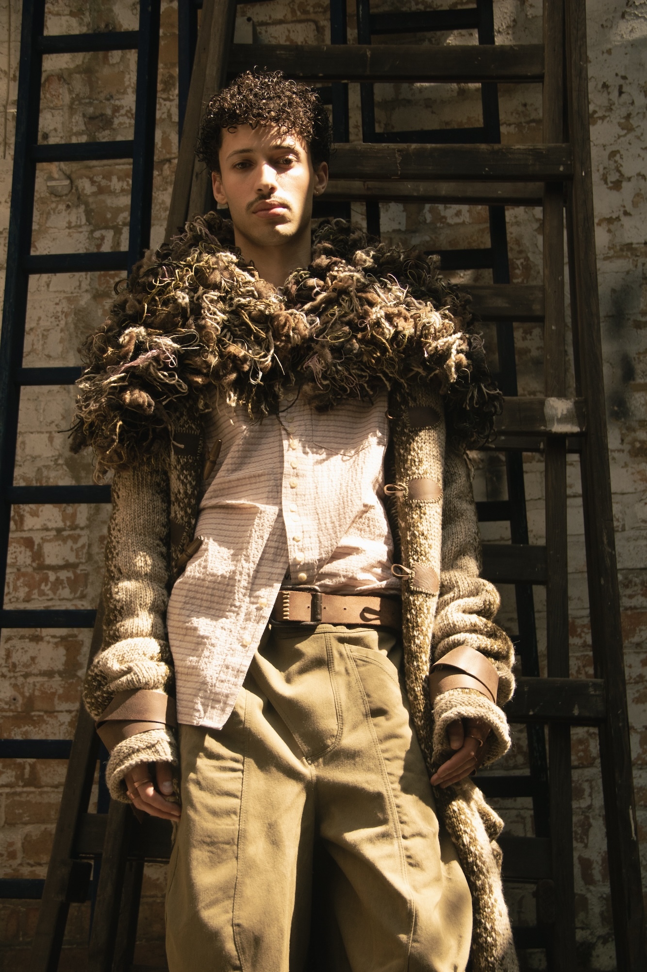 Male model wearing a woollen checkered shirt, half-untucked, and a thick woollen jacket with a large shaggy collar.
