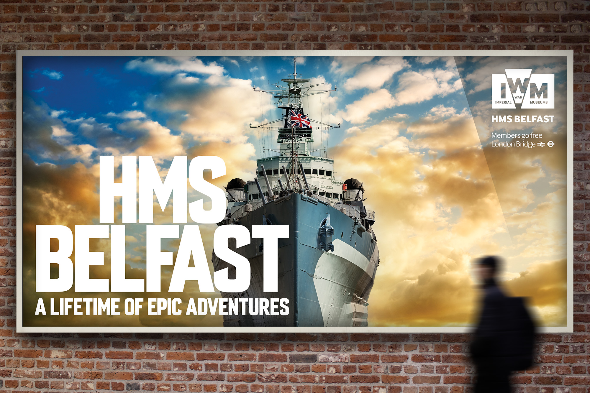 Large wall poster for the Imperial War Museum HMS Belfast exhibition. The poster shows the front of the HMS Belfast ship, and bold white text reading "HMS Belfast a lifetime of epic adventures".