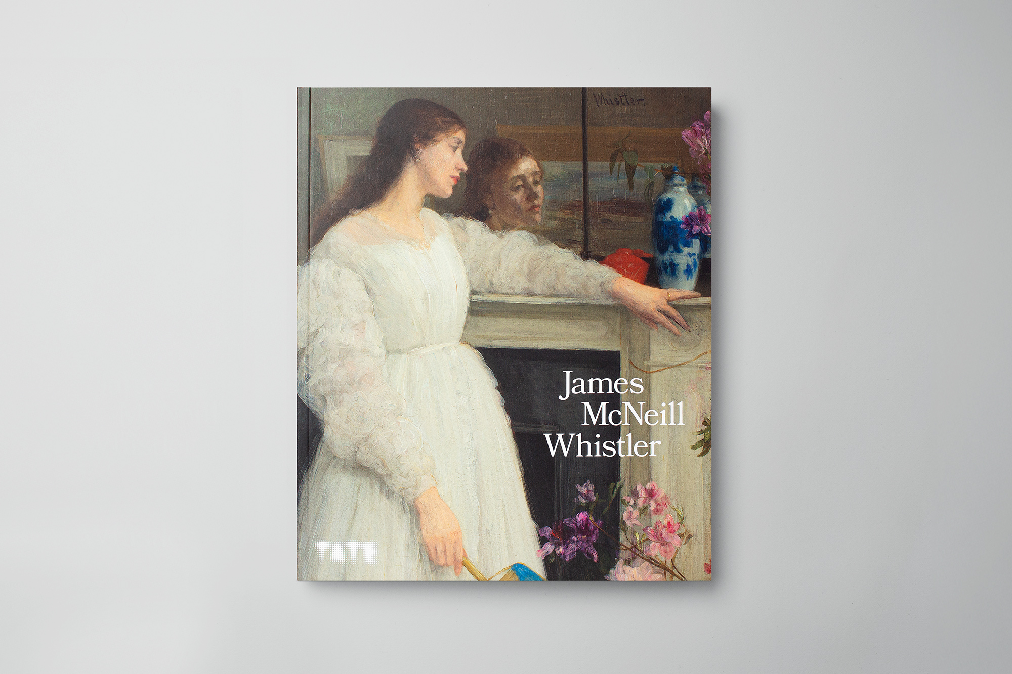 Front cover of a book for the James McNeill Whistler exhibition at the Tate Britain, London, showing an artwork of a woman leaning on a mantlepiece with her face reflected in a mirror.