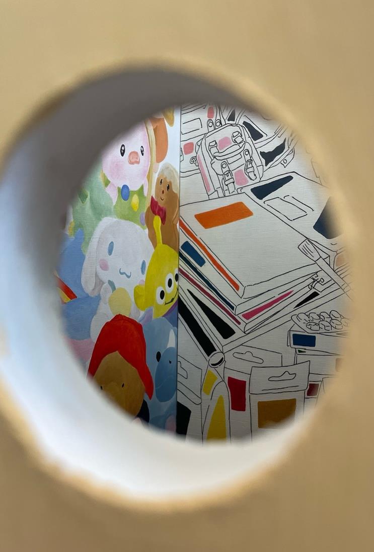 Through a circular opening, a colourful mural featuring cartoonish characters, including a white bear and a yellow creature, is visible on one side, while the opposite side shows a drawing of art supplies in various colours against a white background.