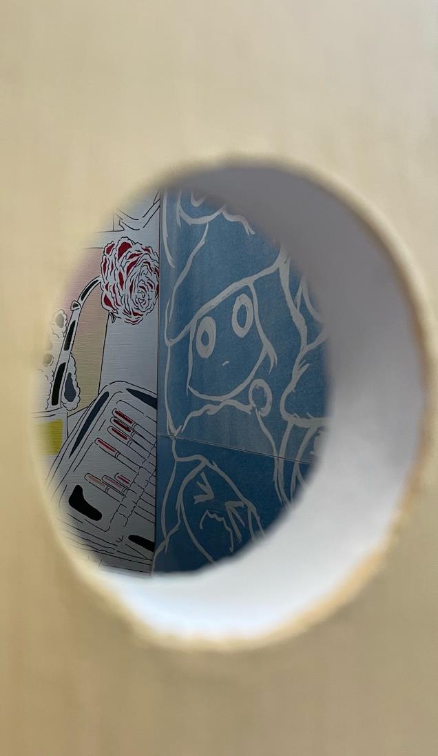 A circular opening in a wooden panel reveals a section of brightly patterned wallpaper featuring abstract designs and illustrations. The blue background contrasts with red floral motifs and various line drawings.
