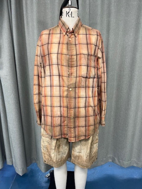 Headless mannequin wearing oversized peach and burgundy plaid shirt with khaki patterned shorts, displayed against grey curtain backdrop.