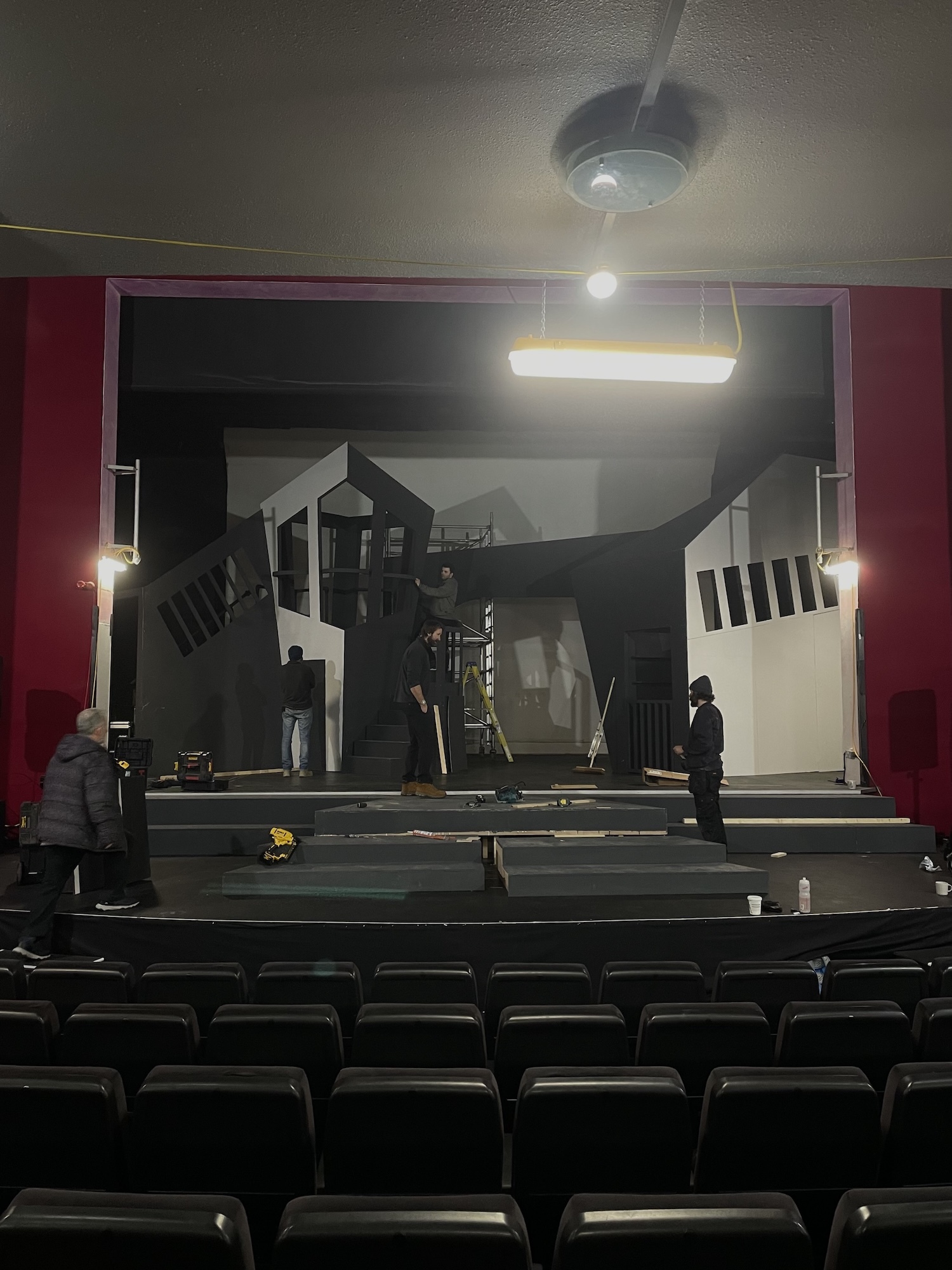 Stage at the Palace Court Theatre, Bournemouth, with multi-level set featuring white and black geometric structures, red proscenium arch, rows of dark seats in foreground.