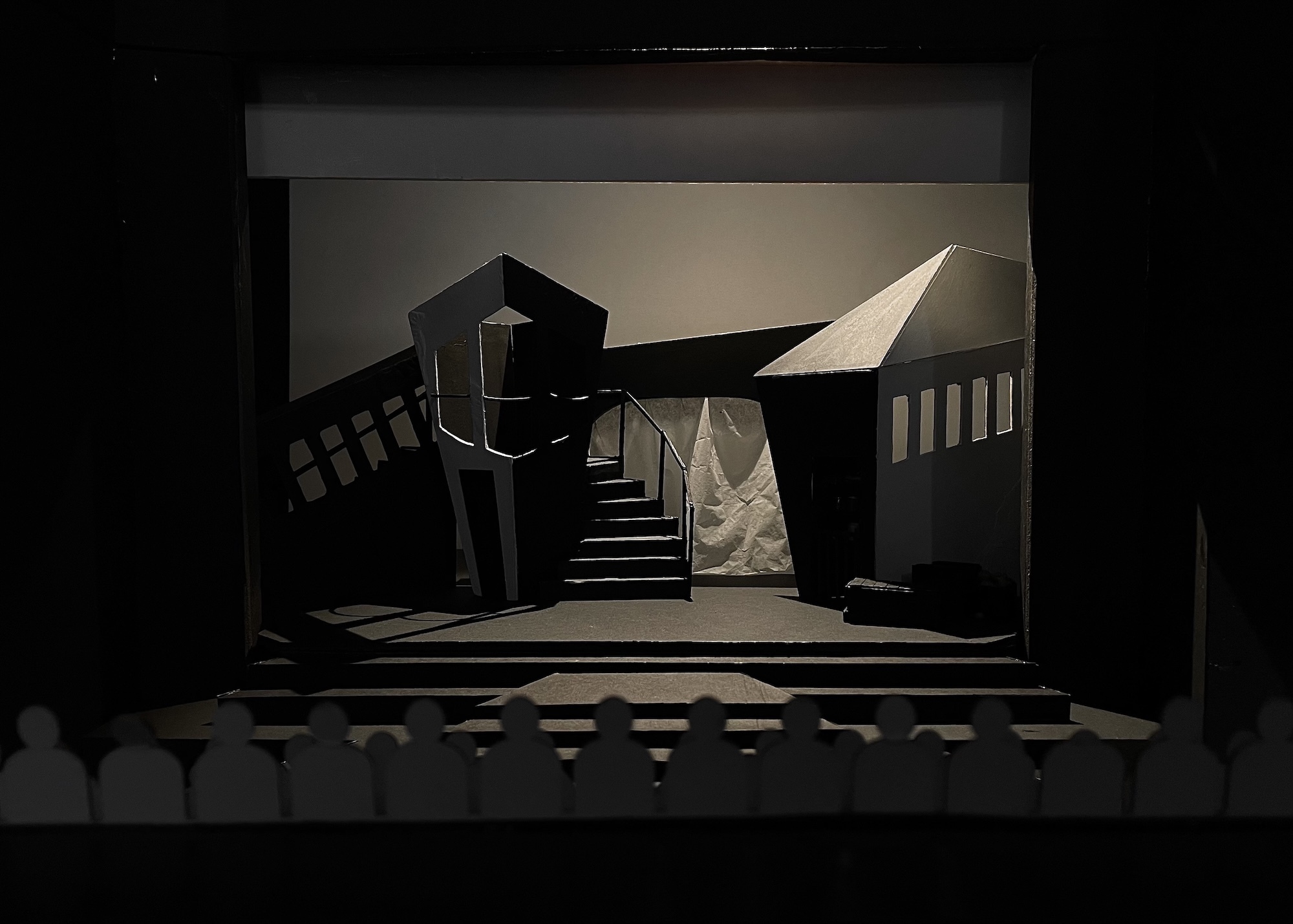 Theatre stage set model featuring geometric black and white angular structures, stairs, and platforms against neutral backdrop with dramatic lighting.