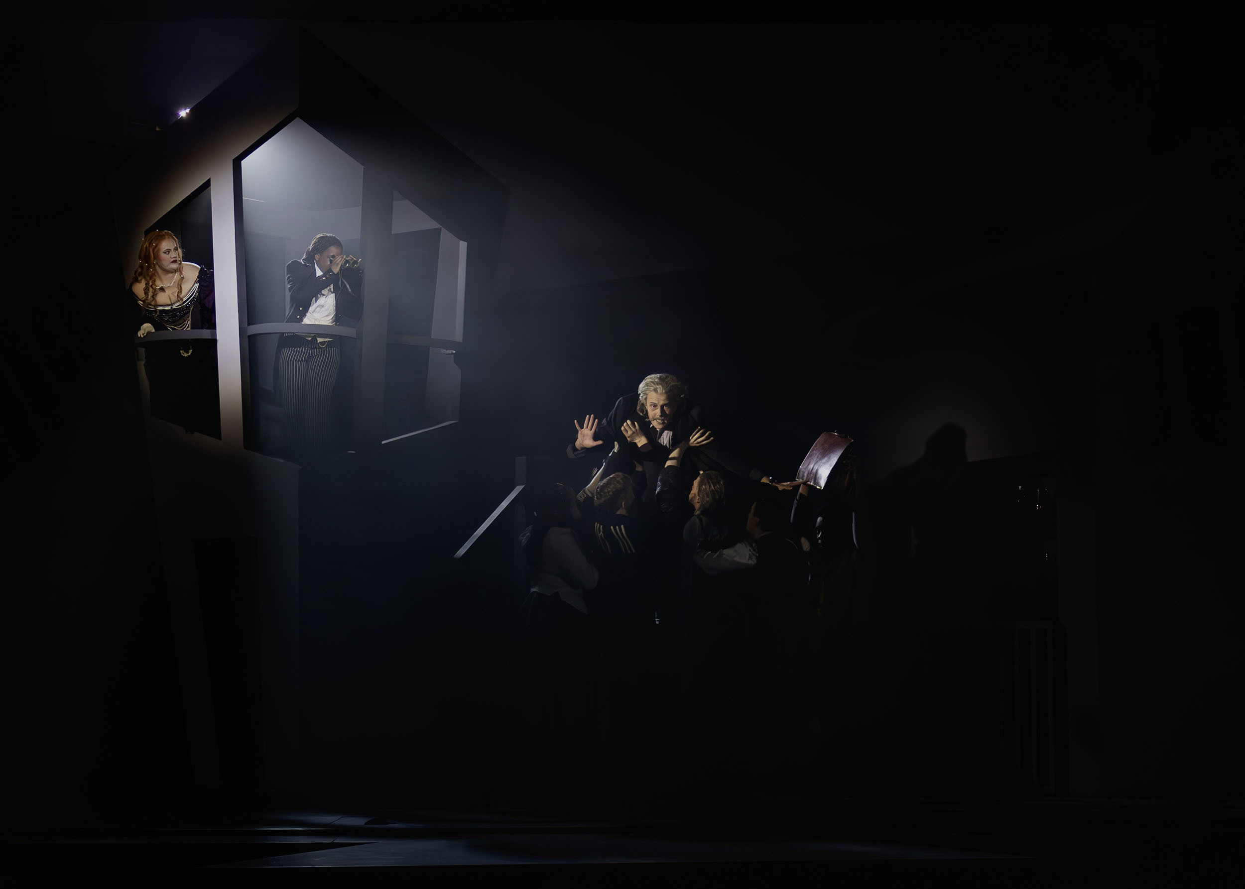 Dark interior with people seated around tables, illuminated by bright white light from windows on left side of frame.