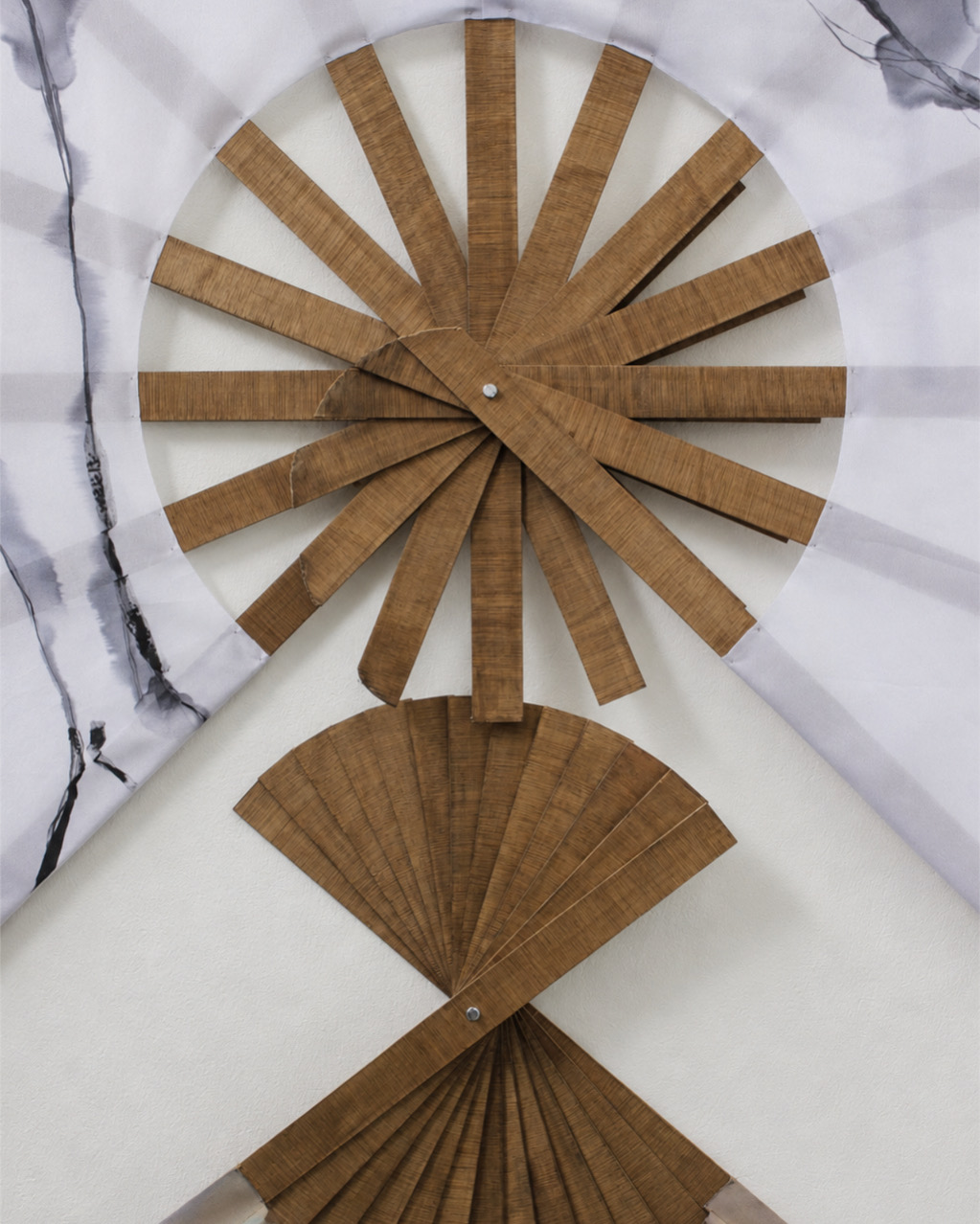 An abstract wall art piece featuring two fan-like shapes made of wooden slats. The upper shape resembles a sunburst, while the lower shape is curved, both set against a light-coloured background with hints of marble texture.