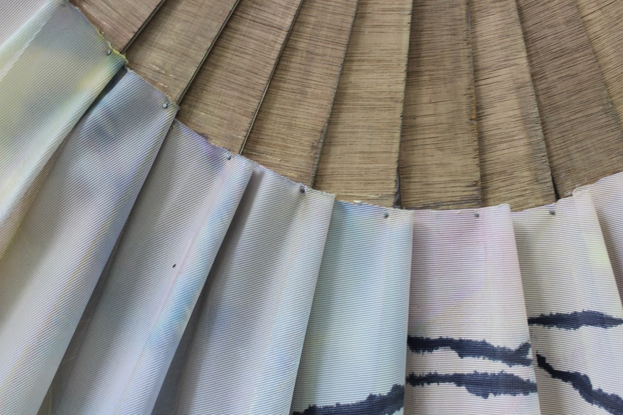 A close-up view of a decorative fan, featuring alternating bamboo and fabric segments. The fabric has soft pastel colours and abstract patterns, while the bamboo showcases a natural texture.