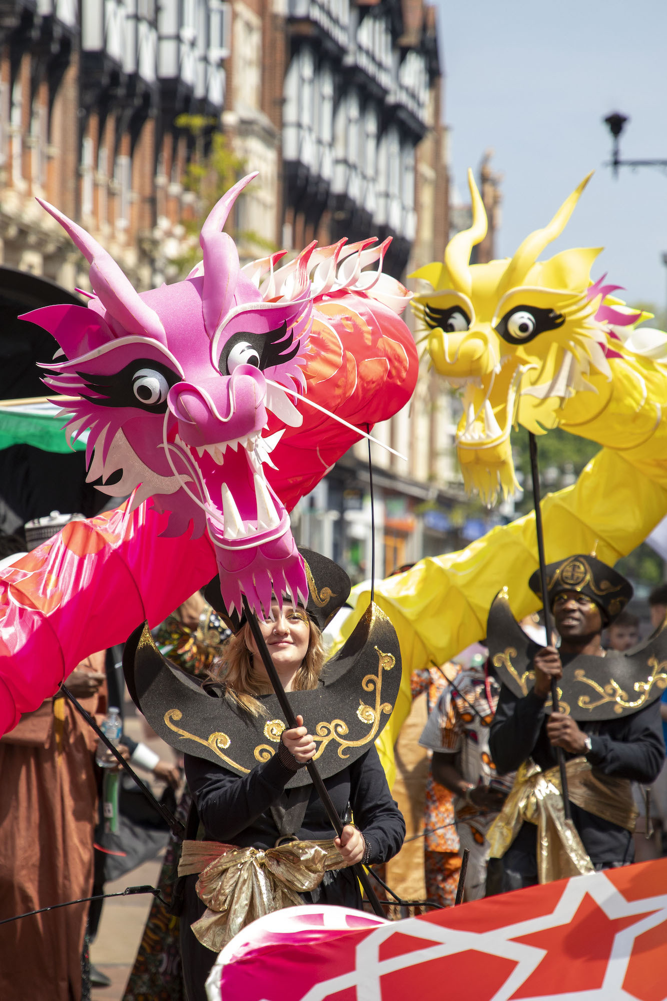 Performers dressed in black and gold costumes carrying colourful Chinese-inspired dragon puppets on sticks.