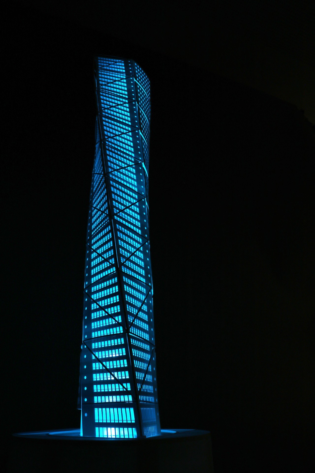 Model of a blue illuminated high rise building, dark background.