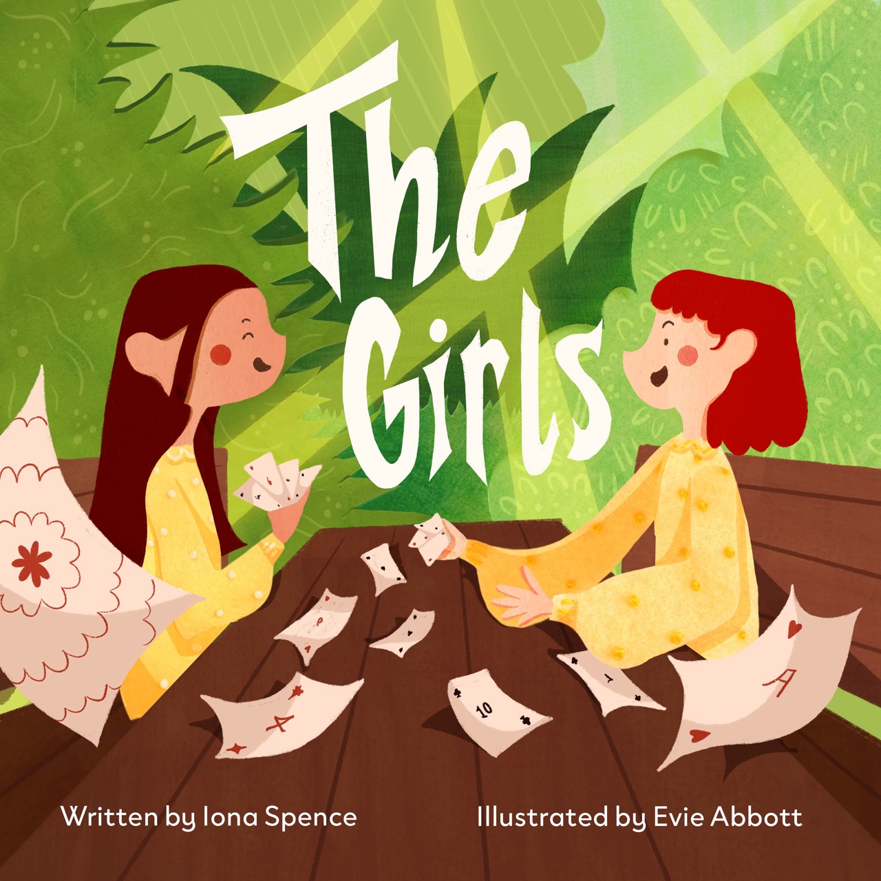 Two girls sitting on a wooden surface, engaged in a card game. One girl, with wavy hair and a yellow top, holds cards while the other, with curly red hair, is reaching for her cards. The background features lush green foliage.