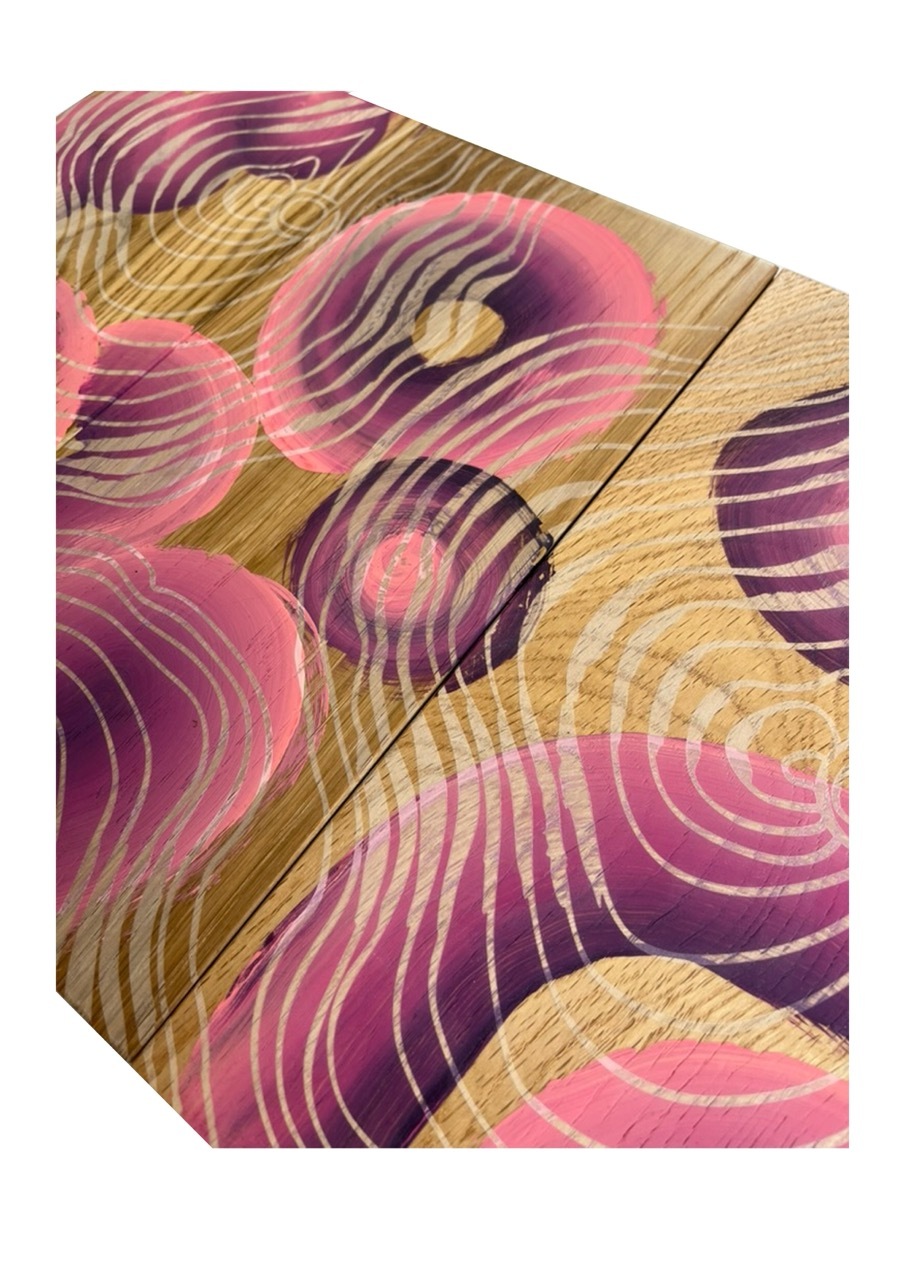 Abstract geometric composition with overlapping circular shapes in pink, purple, and gold tones on wooden textured background.
