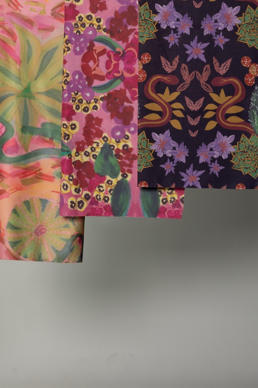 Overlapping decorative papers with floral patterns in pink, purple, green and yellow tones on grey surface.