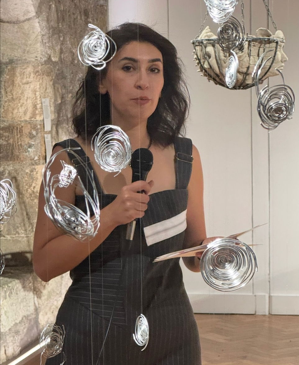 Woman with dark hair in black sleeveless dress holding phone, taking mirror selfie. White spiral drawings overlaid on image.