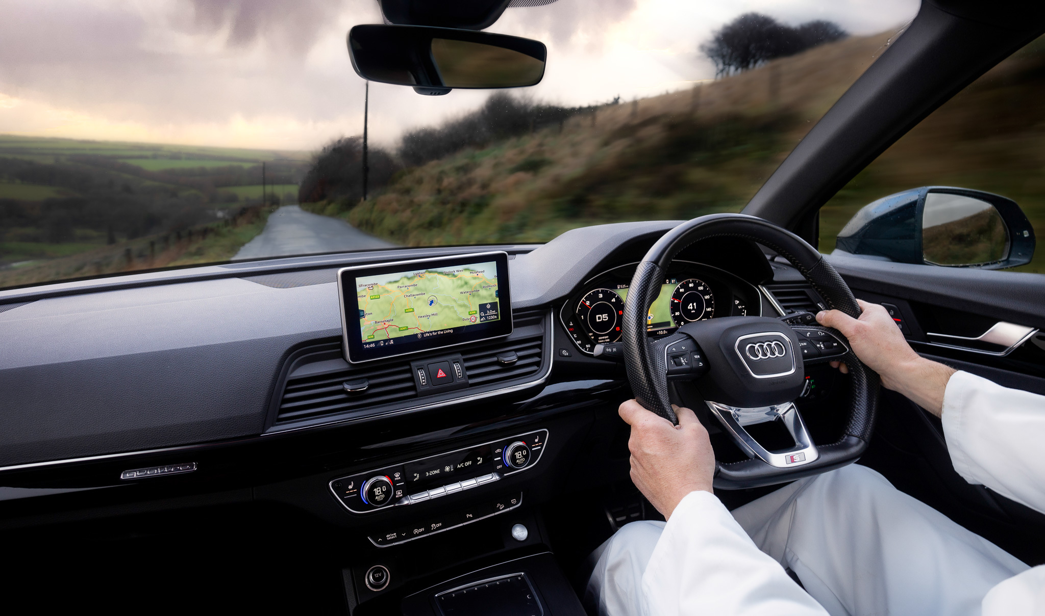 An interior view of a person driving a modern car with a rural view.