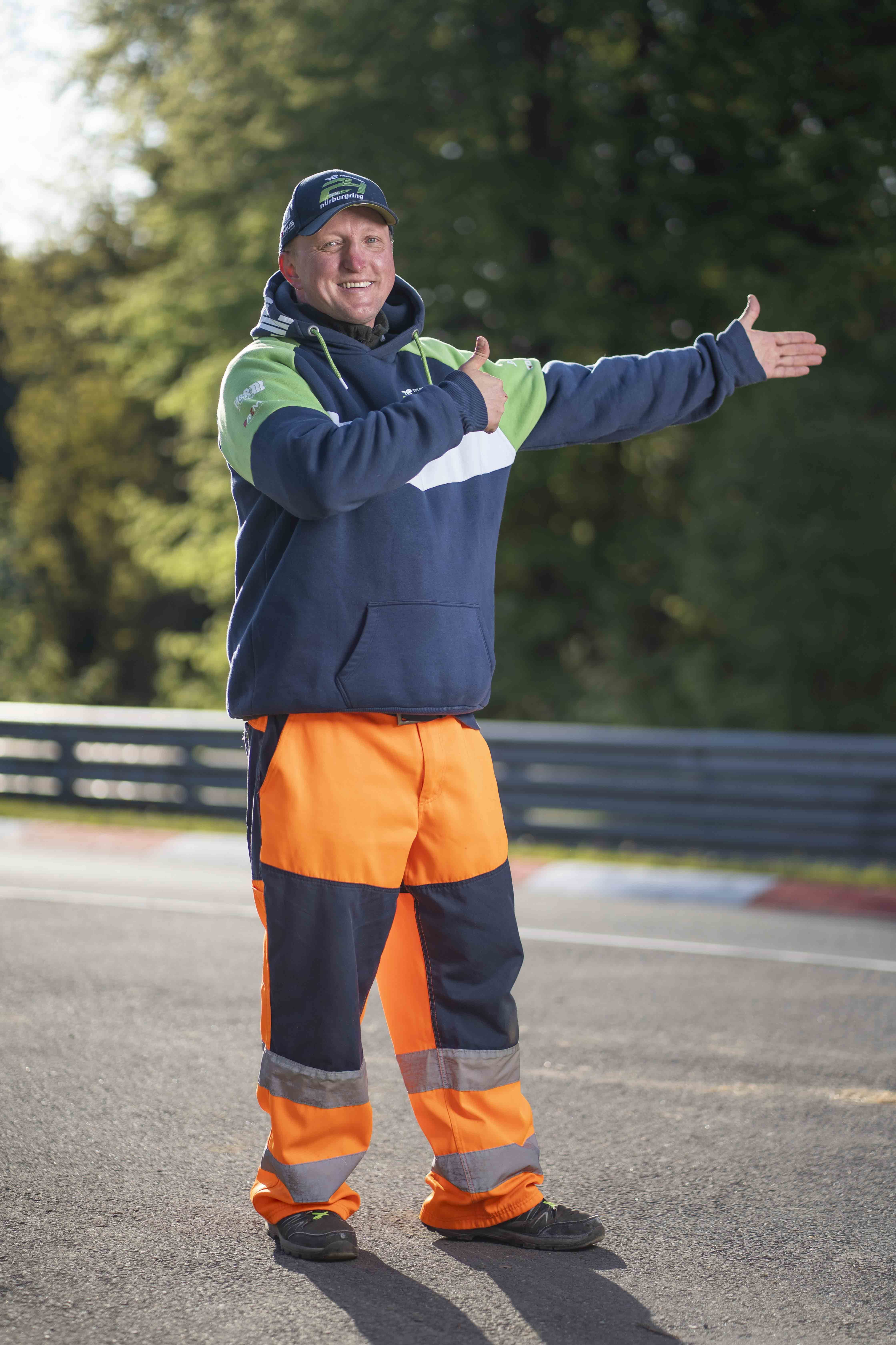A man directs traffic, wearing orange high-vis trousers.