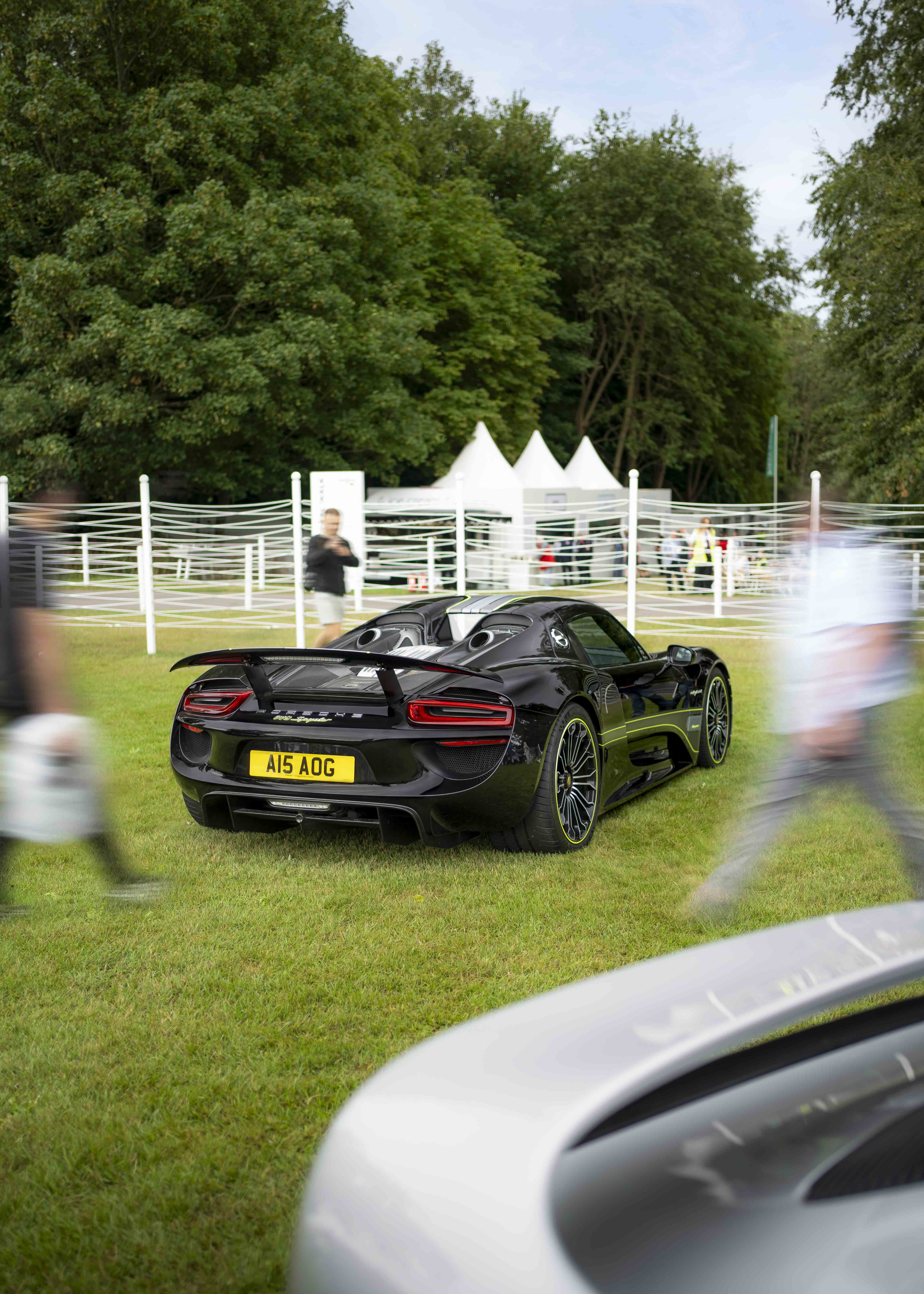A black Porsche on the grass surrounded by long exposures of people.