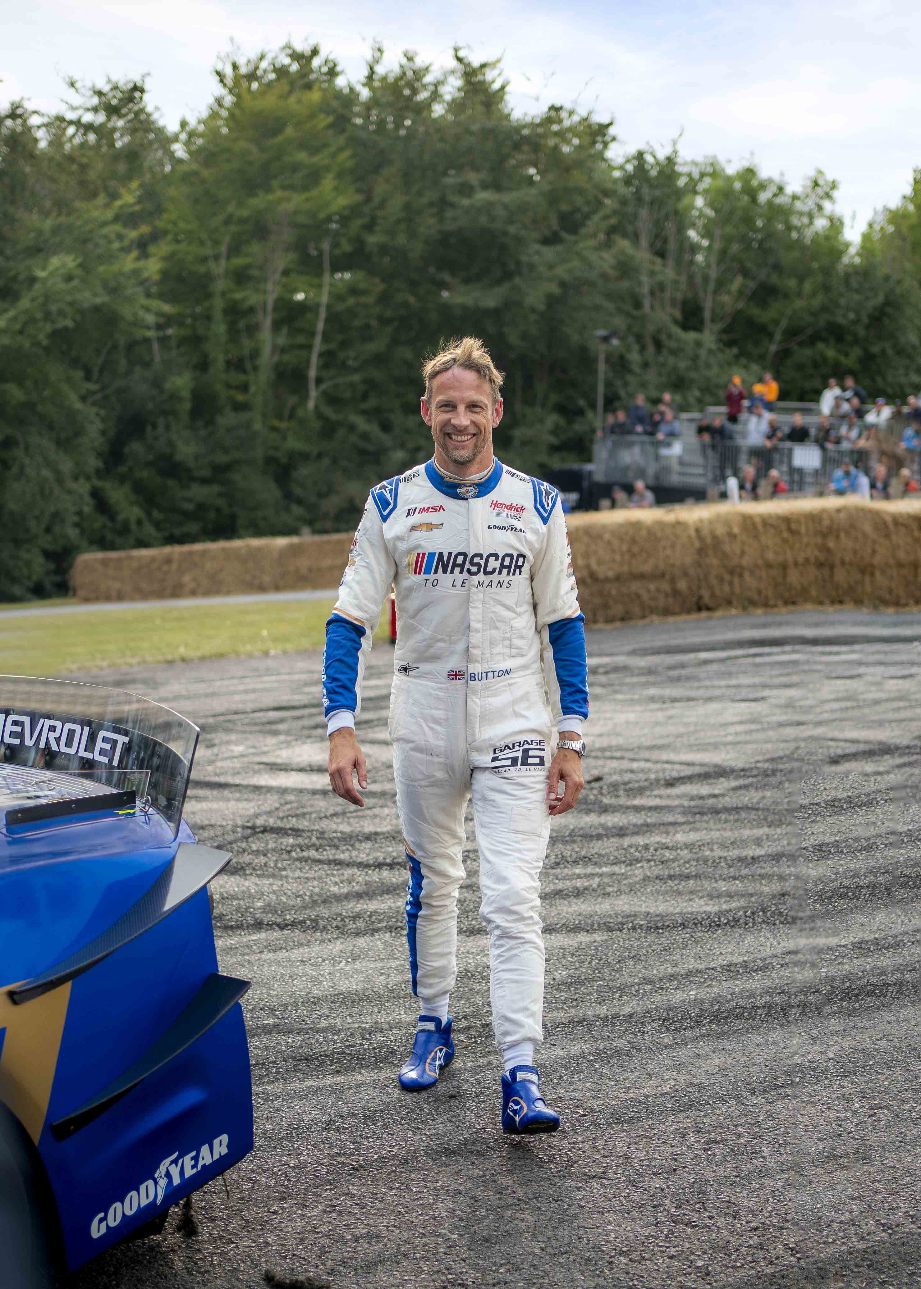 A man in a white NASCAR suit on a racetrack.