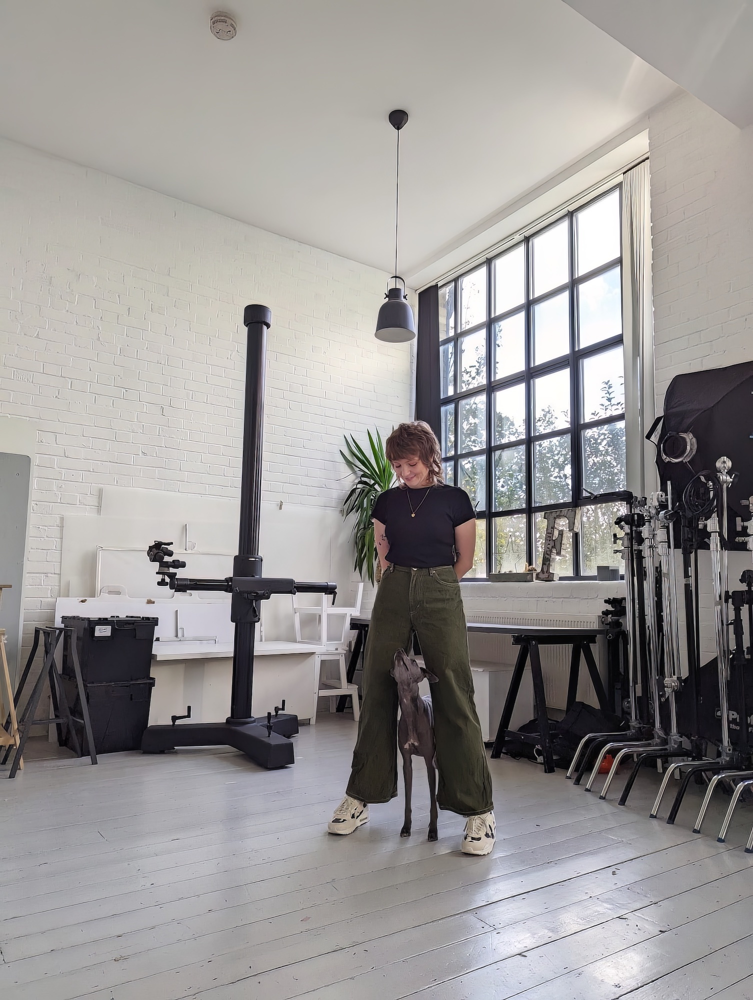 Photographer Frankie Turner standing in her studio with her dog between her legs.