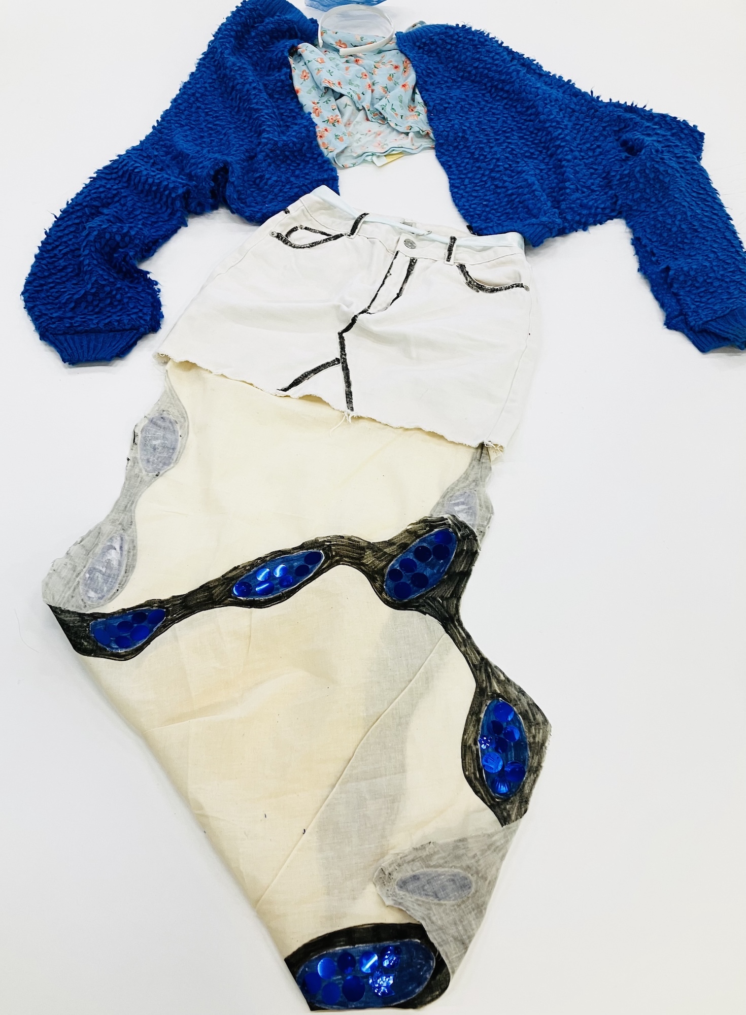 Blue cardigan, white top with black line drawing, cream skirt with blue oval gems and grey pattern on white background