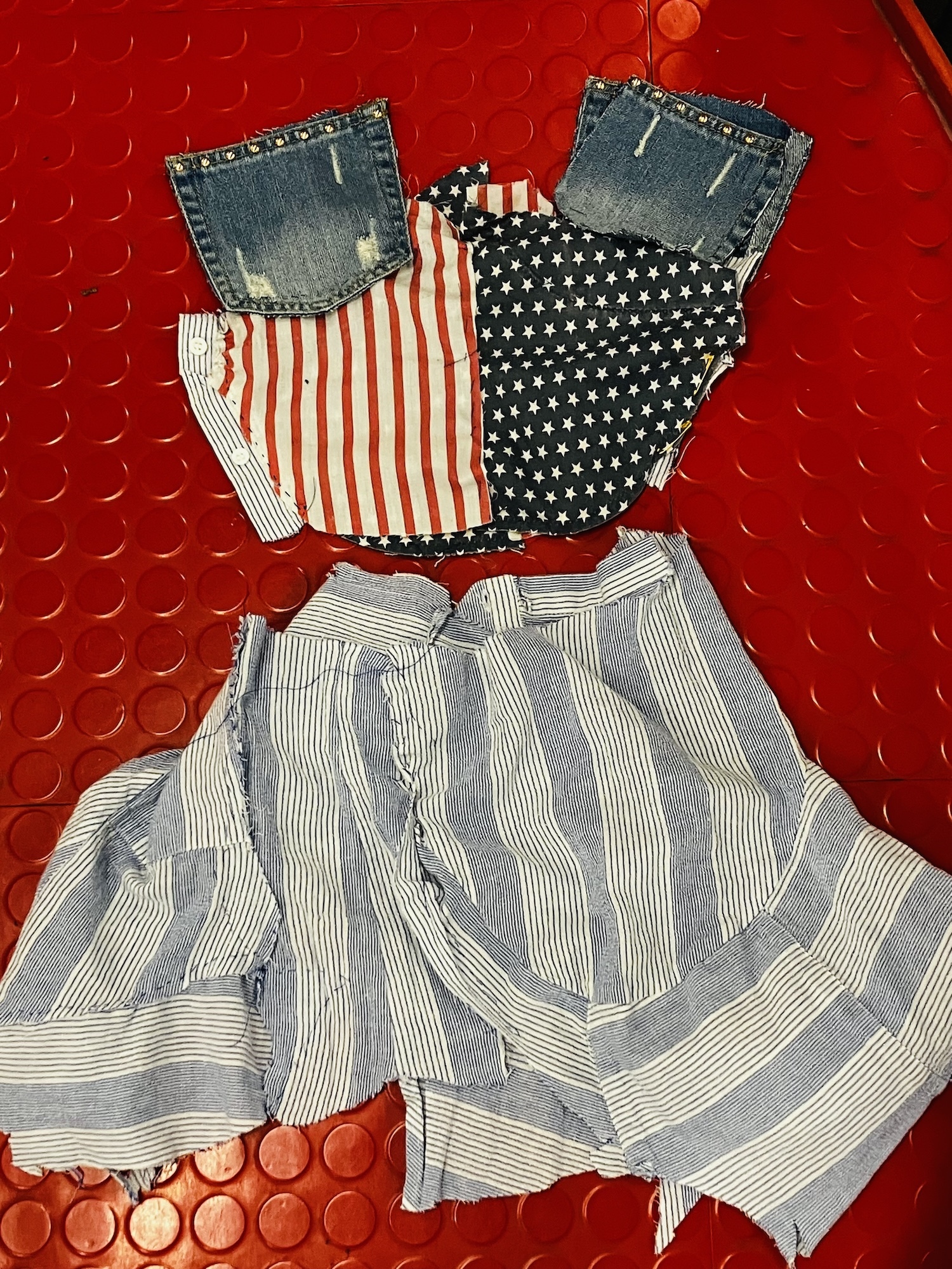 Two denim-topped garments with red striped and star-patterned fabric, plus grey striped shorts on red textured surface