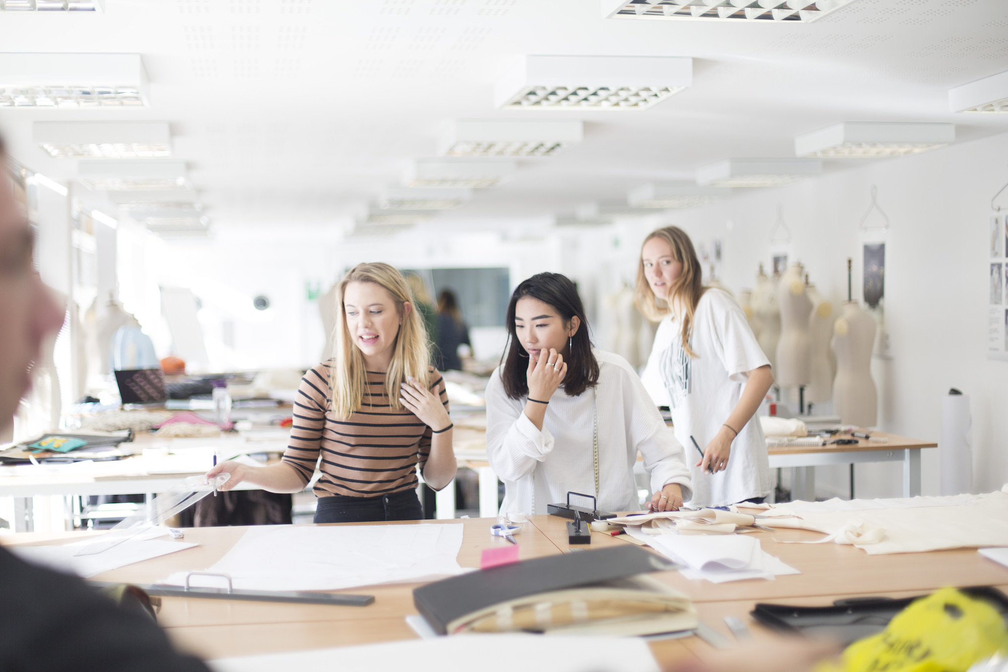 Three BA (Hons) Fashion students working with fabrics in a classroom.