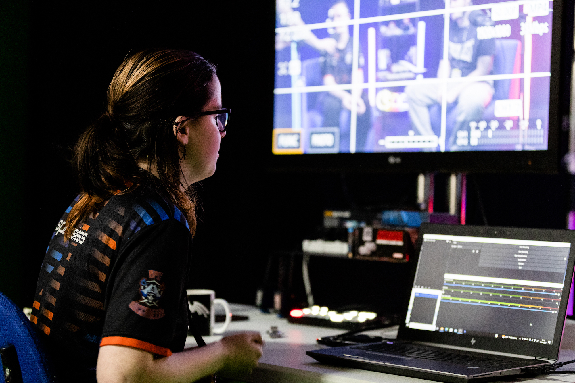 A Bournemouth and Poole College student in a studio watching a monitor with a laptop in front of them during a broadcast production.
