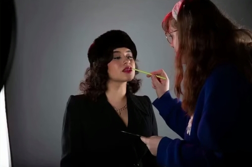 Kasandra Georgi having red lipstick applied to her.