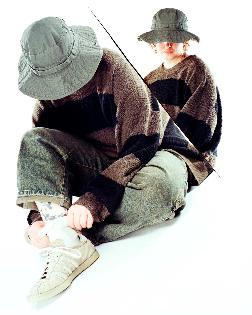 A person wearing a grey bucket hat and a brown striped oversized sweater sits with one leg bent. They are adjusting their white shoe, while a reflective surface displays a mirrored image, showing the same person from a different angle.