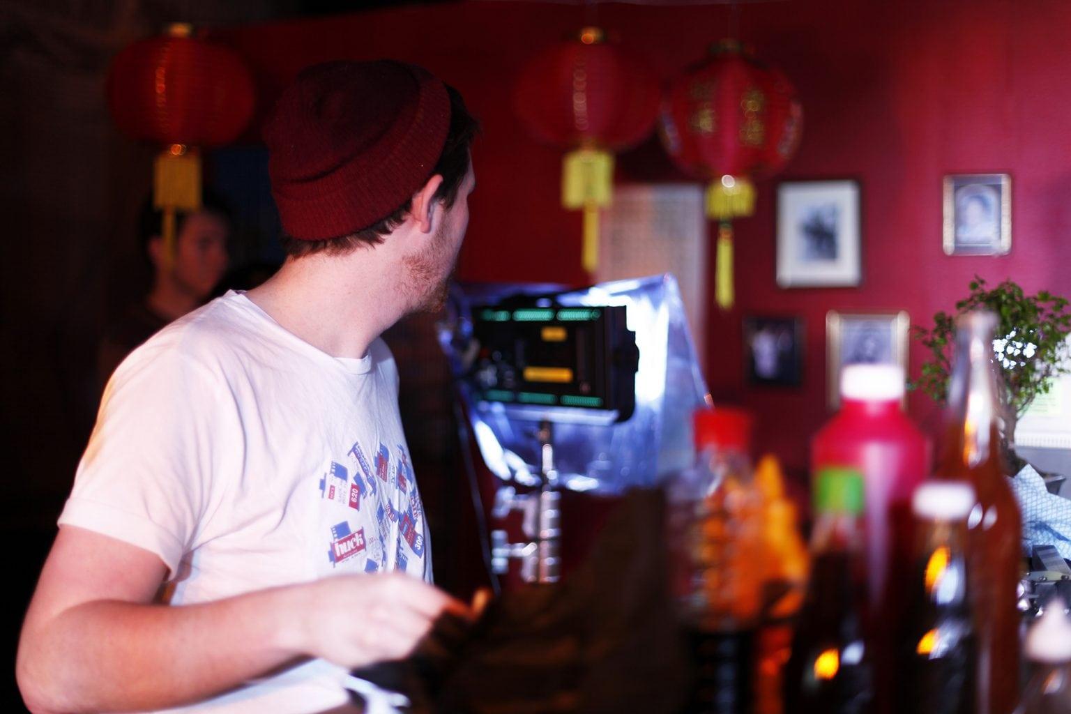 A person viewed from behind using a film camera in a dim-lit room with Chinese-style lanterns in the background.