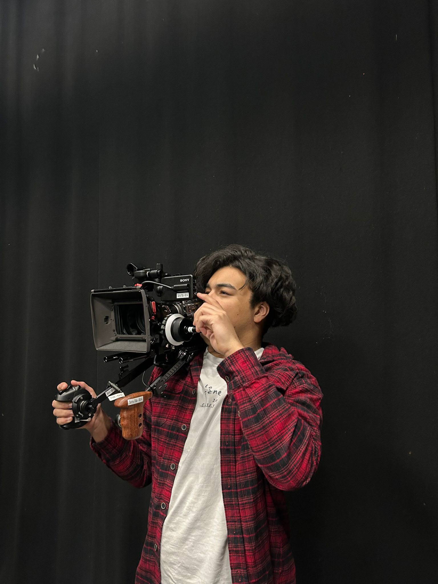 F Gibbs holding a large film camera with a black curtain backdrop.