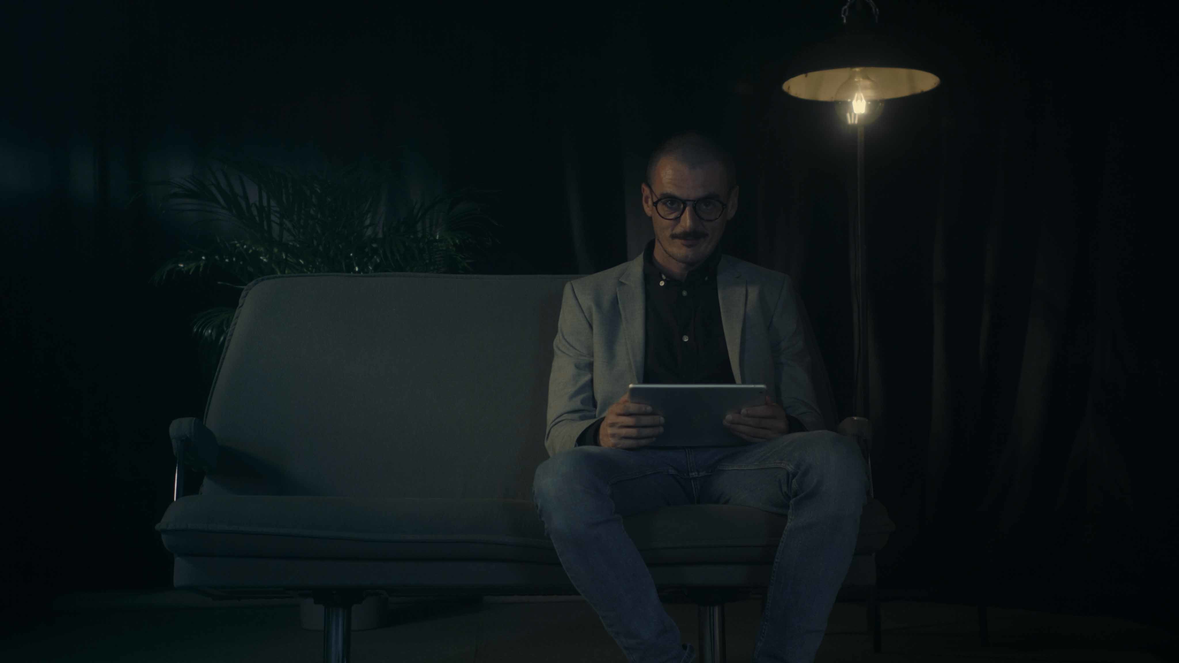 A seated man with a tablet computer looks into the camera