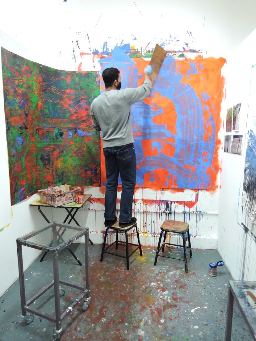 A student painting on a large canvas stood on a stool in the art studio