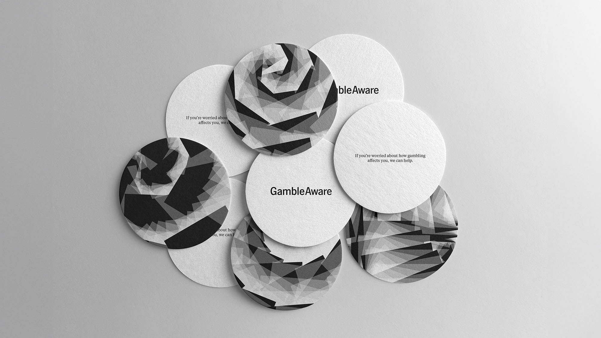 Circular white cards with black geometric patterns arranged in overlapping cluster, some featuring "GambleAware" text, on grey surface.